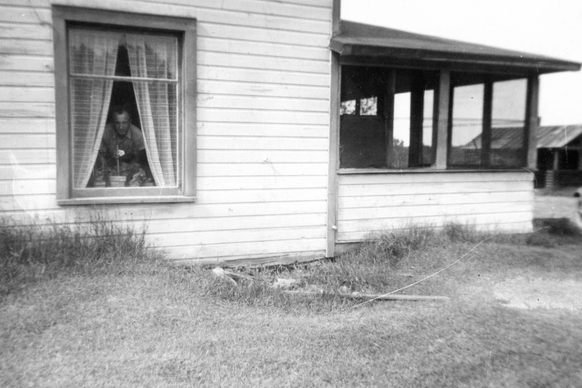 "Taken from the south side of the house, how do you like my geraniums, that in the window is my husband, in the distance is John's cabin, I call it his work-shop, it's cosy inside and nice. June 12, 1946"