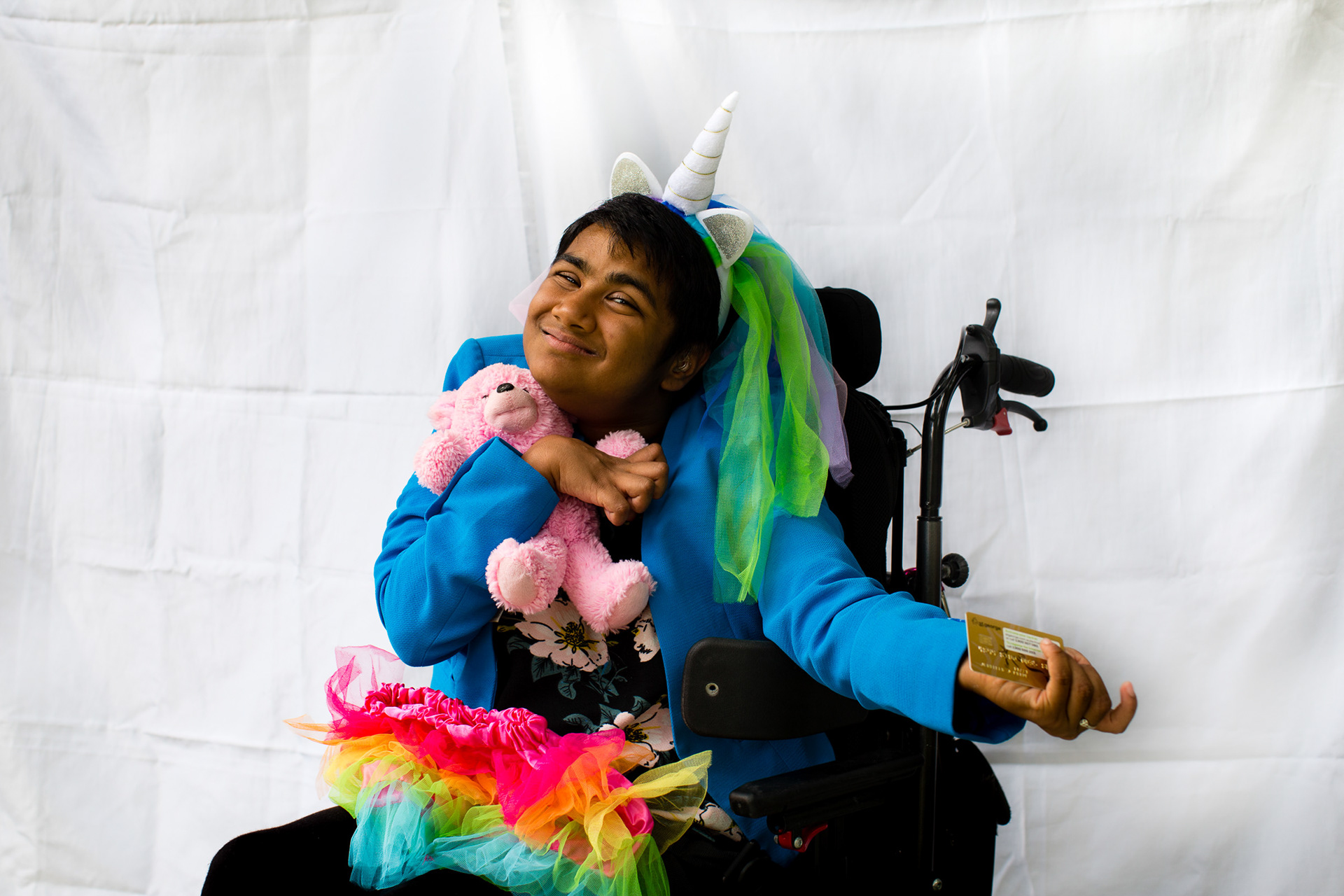 Marusha wearing a colourful tutu, a unicorn headress, clutching a pink bear and holding a gold credit card