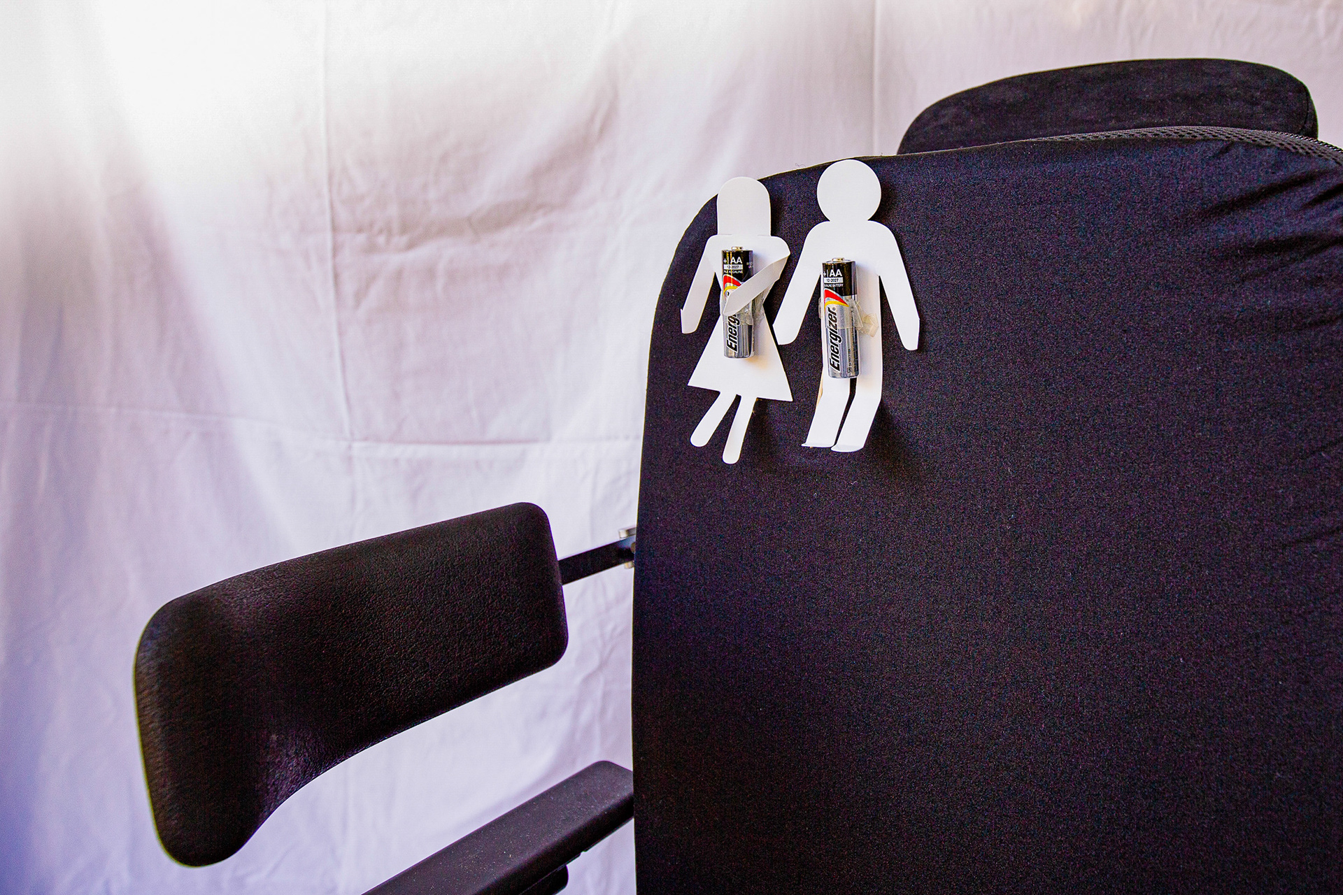 2 cutout paper figures with a battery for a body, stuck to a wheelchair