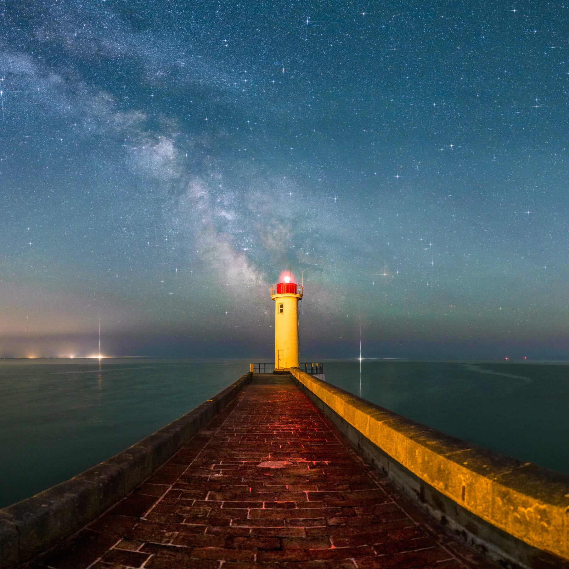 La digue du Raoulic est orientée nord-sud, donc elle se prolonge en direction du centre galactique, c'est-à-dire le coeur de notre galaxie, là où la Voie lactée est la plus spectaculaire. Le môle sépare la constellation du Scorpion (à droite) de celle du Sagittaire. Remarquez la silhouette d'un cheval sombre qui cabre juste au-dessus du phare. Les lumière blanches à l'horizon tout à gauche sont celles de Penmarc'h et Saint-Guénolé. L'ajout d'un filtre "star" devant l'objectif permet d'obtenir ces jolies aigrettes autour des sources de lumières les plus brillantes. J'ai fait en sort qu'elles ne soient pas présentes autour de la lanterne rouge du Raoulic.