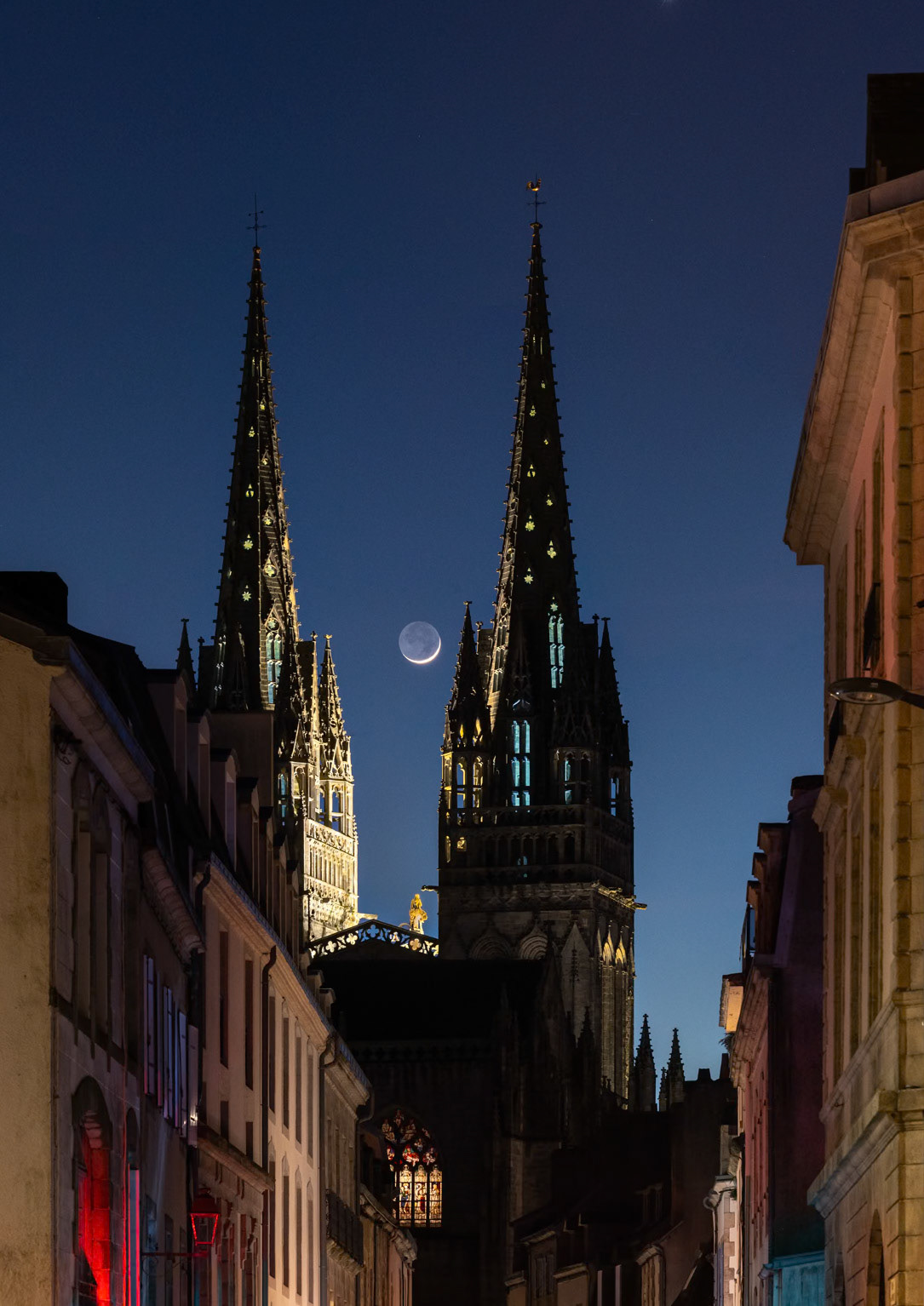 Ce soir, la Lune en Croissant parée de sa lumière cendrée se pavane dans les lueurs du crépuscule. Depuis le début de la rue des Réguaires, la perspective s'ouvre sur la Cathédrale Saint-Corentin qui est encore éclairée, ce qui lui donne du relief. Les feux tricolores du carrefour offrent quelques touches de vert et de rouge.