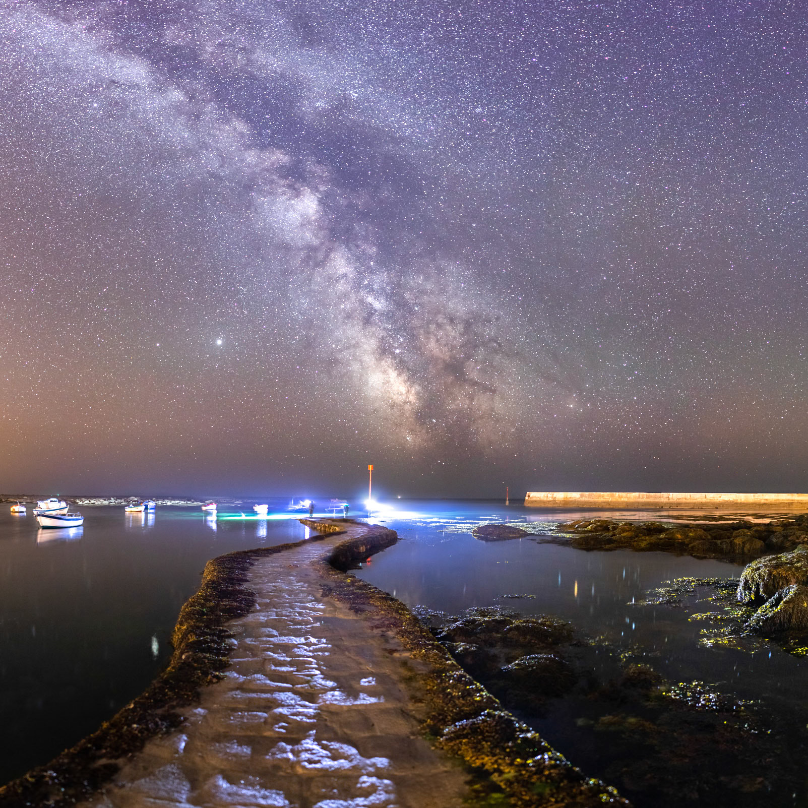 La cale de Saint-Pierre nous mène à prendre notre envol parmi les étoiles de la Voie lactée qui est superbe face à l'océan. Des pêcheurs qui s'affairent au bout de la cale éclaire efficacement le premier plan qui gagne en contraste et relief.
