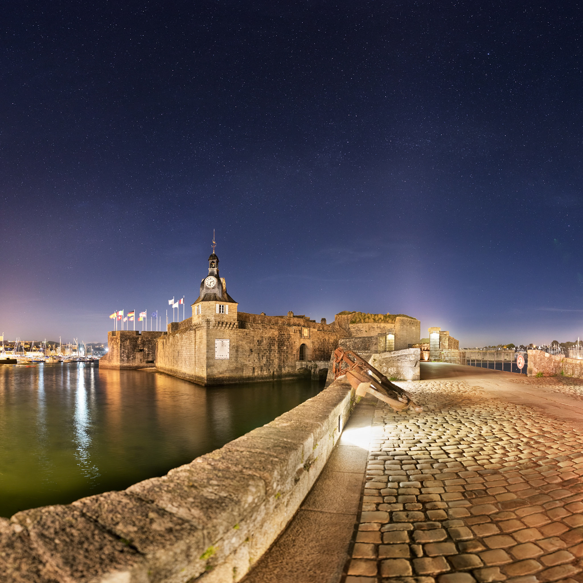 Les lumières des éclairages publics associées aux lumières du port font de Concarneau une ville où la Voie lactée n'est guère visible. Elle est réduite ici au pied de la Ville Close à une très pâle lueur dans un ciel bien bleu grace à la présence de la Lune.