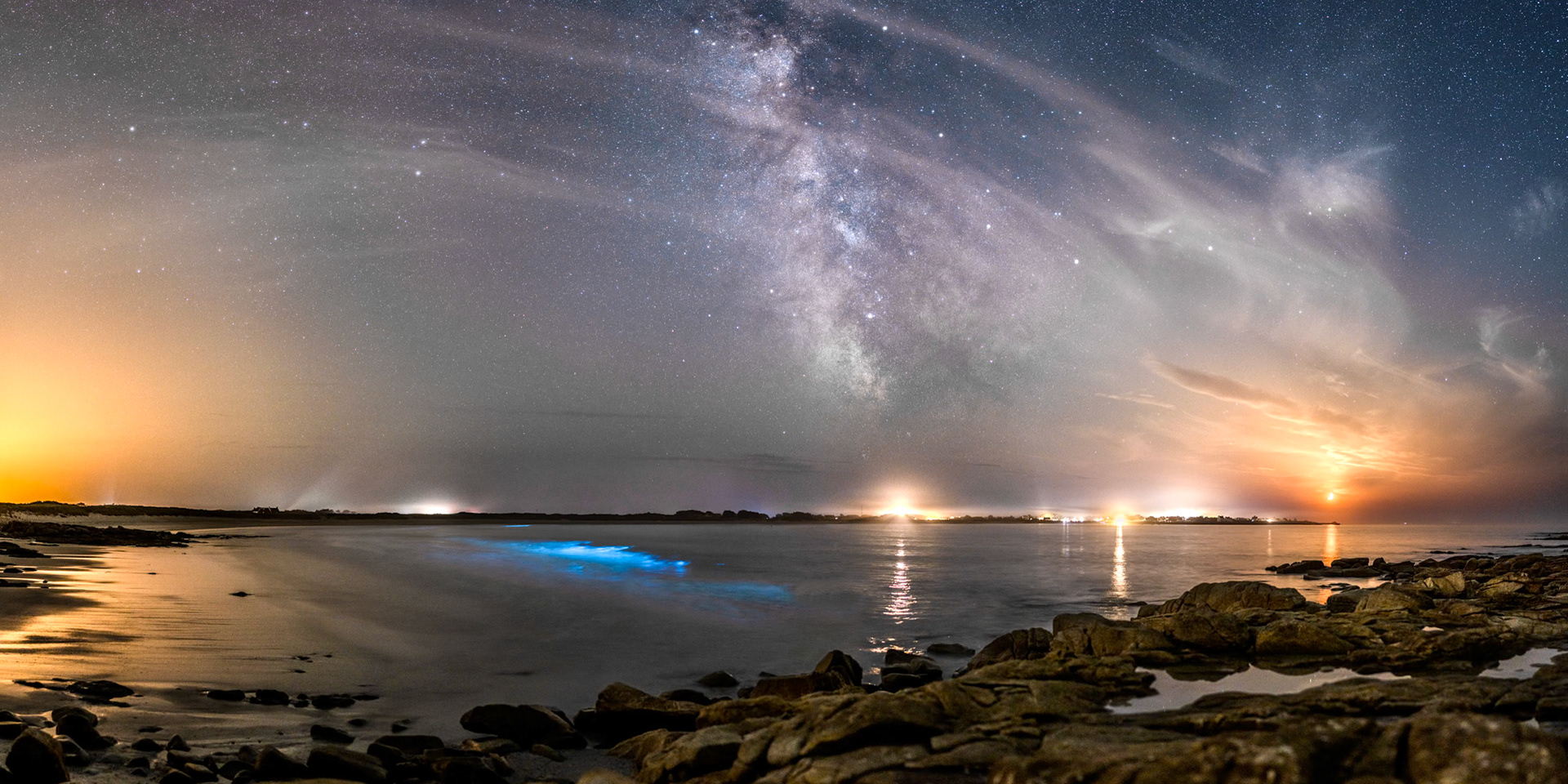 Du plancton phosphorescent (de la bioluminescence) a fait son apparition depuis quelques jours dans la Baie de Pors Carn. Installé sur des rochers au sud de la Pointe de la Torche, je prend un peu de hauteur pour mieux voir les vagues déferlantes qui font apparaître la lueur bleutée (invisible à l'oeil nu qui perçoit péniblement les couleurs de nuit). De gauche à droite, on peut voir la lumière orangée du Guilvinec, la lumière d'une voiture au-dessus du plancton, le puissant phare d'Eckmühl  et la paillote "Chez Marie-Cath" juste à gauche de la lueur blache du port de Saint-Guénolé, et enfin, le disque orangé d'un Quartier de Lune en train de se coucher. Dans le ciel, des cirrus remplissent une voûte déséquilibrée par une Voie lactée trop verticale en cette saison.