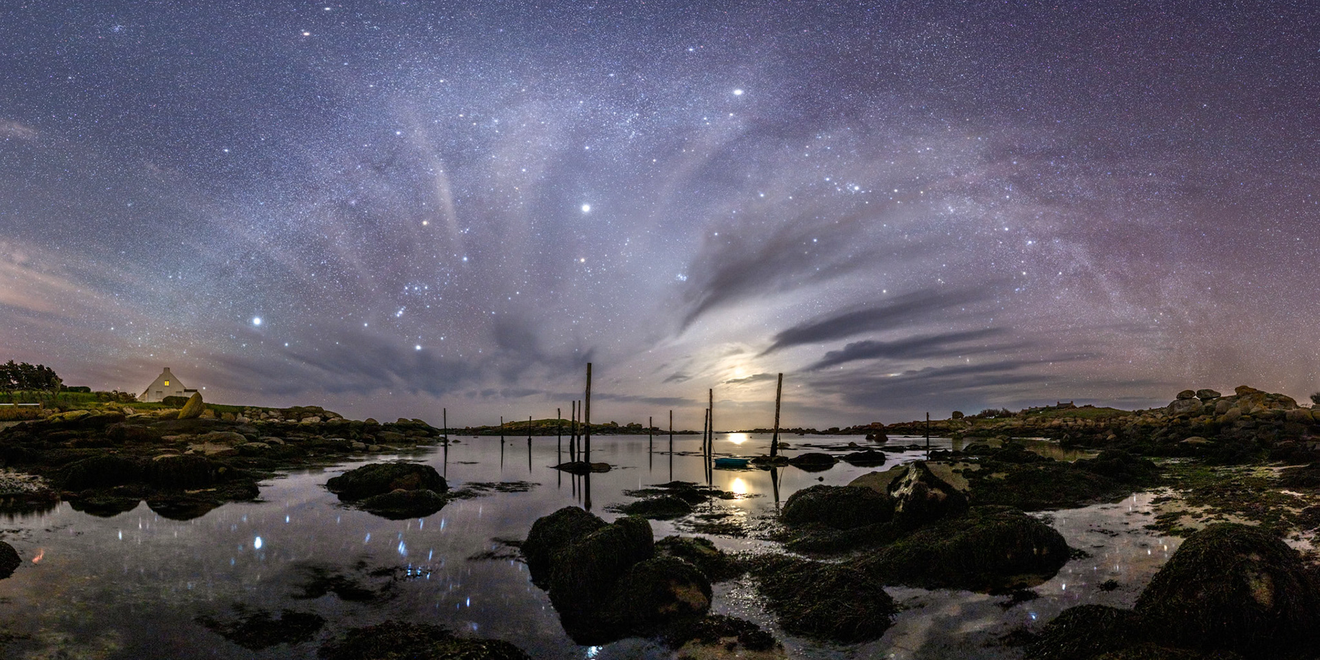 Les nuages qui auraient pu ma masquer la Voie lactée sont au contraire un atout : ils forment comme les rayons d'une roue et leurs nuées diffusent la lumière des étoiles les plus brillantes. Hélas, un léger vent empêche la formation de beaux reflets dans l'eau qui entoure les rochers dégagés par la marée qui se retire. La présence de la Lune apporte un peu de lumière dans ce lieu dépourvu de pollution lumineuse. Cela aurait aporté de la chaleur qui aurait fait du bien ! Mais cette relative austérité confère à la photo plus de force.