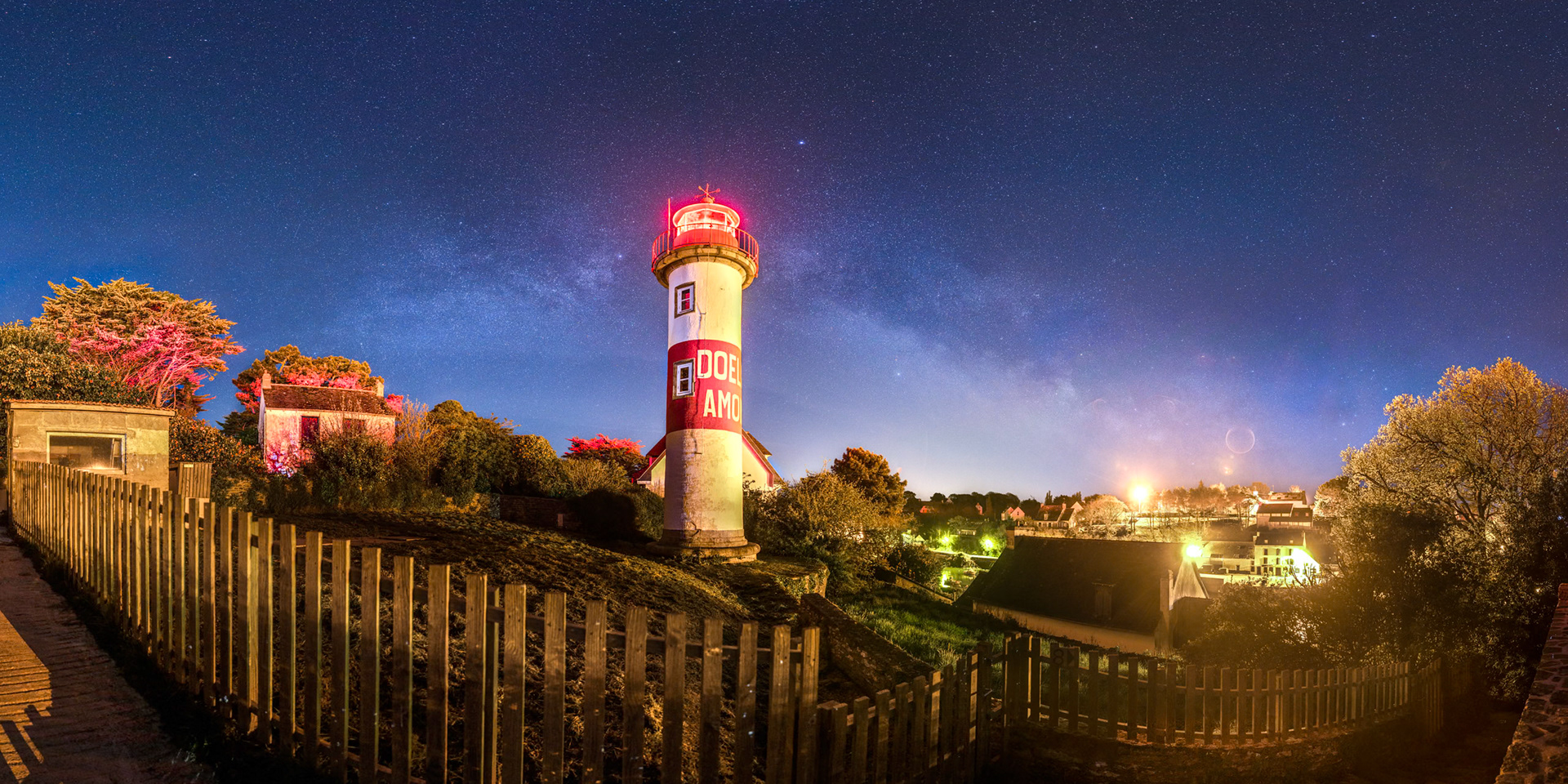 Malgré l'intense pollution lumineuse qui règne dans le port de Doëlan, la Voie lactée demeure visible. Elle passe derrière le phare qui projette de la lumière rouge sur les arbres situés tout à gauche.