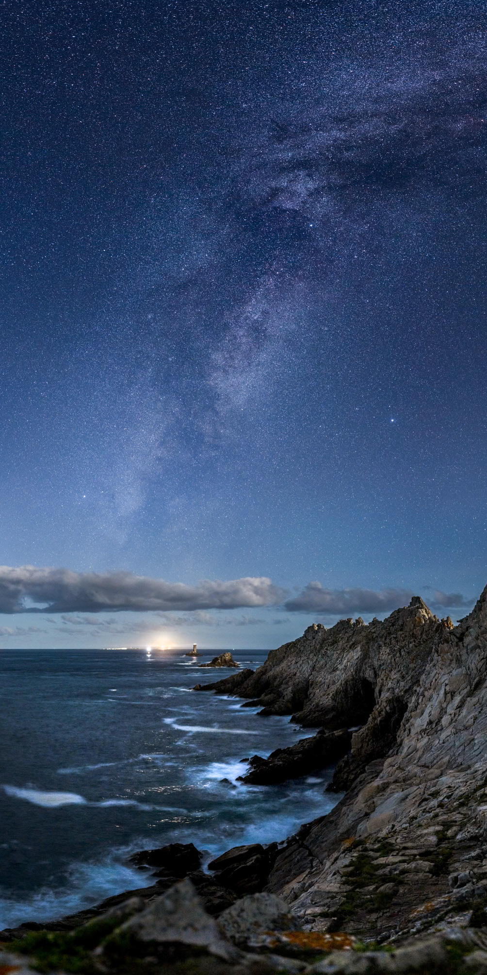 La Voie lactée se dresse à la verticale de l'Île de Sein. Un gros Croissant de Lune qui se lève dans mon dos illumine les crêtes des falaises de la Pointe du Raz et teinte le ciel en bleu. La lumière du phare de Sein zébre l'océan en dessous de celui-ci.