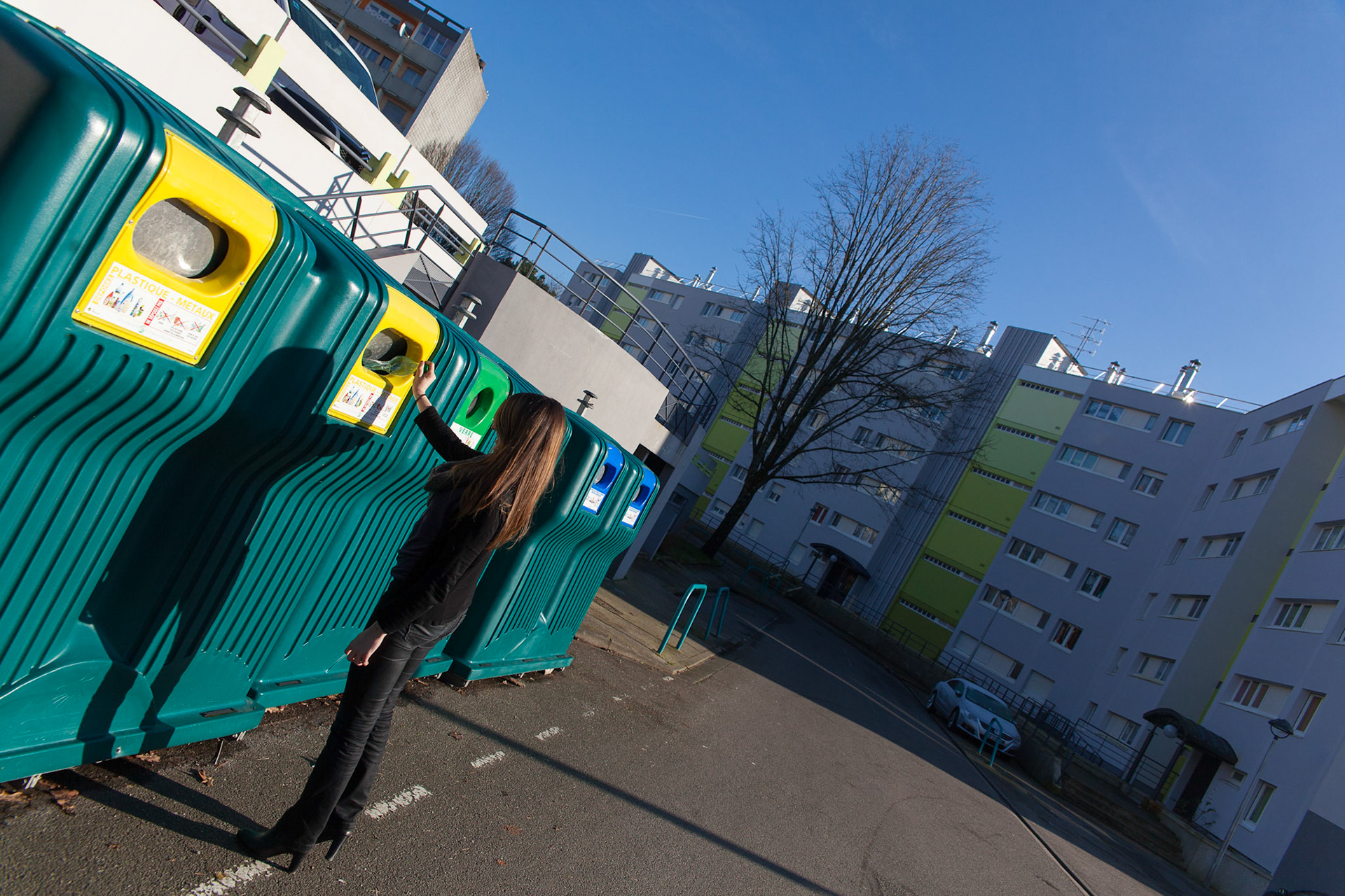 Une jeune femme dépose une bouteille en plastique dans le container prévu à cet effet situé derrière la maison des services publics.