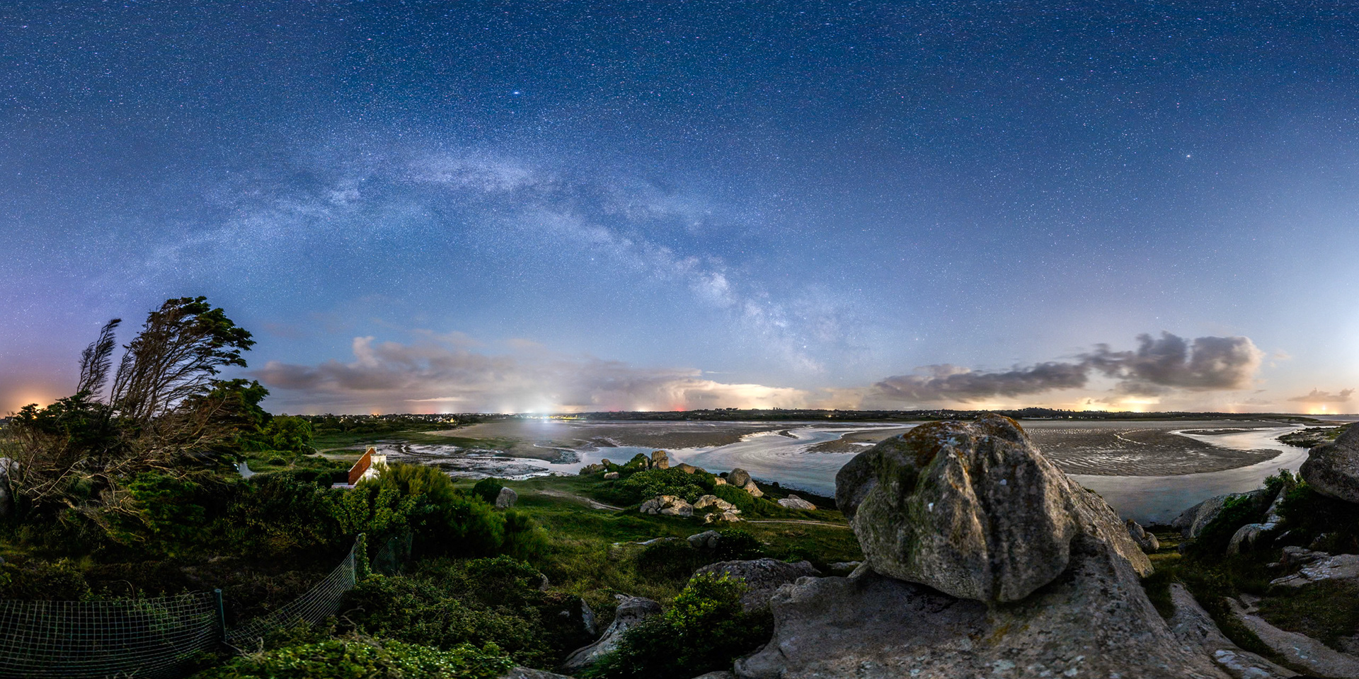 Tout à gauche, un cyprès nous entraîne vers la Voie lactée qui rejoint un gros rocher, point culminant de la Baie de Kernic. Sous l'arche galactique, la lumière vive du Casino de Plouescat et des nuages qui longent l'horizon. Le tout est illuminé par un Quartier de Lune situé hors champ tout à droite.
