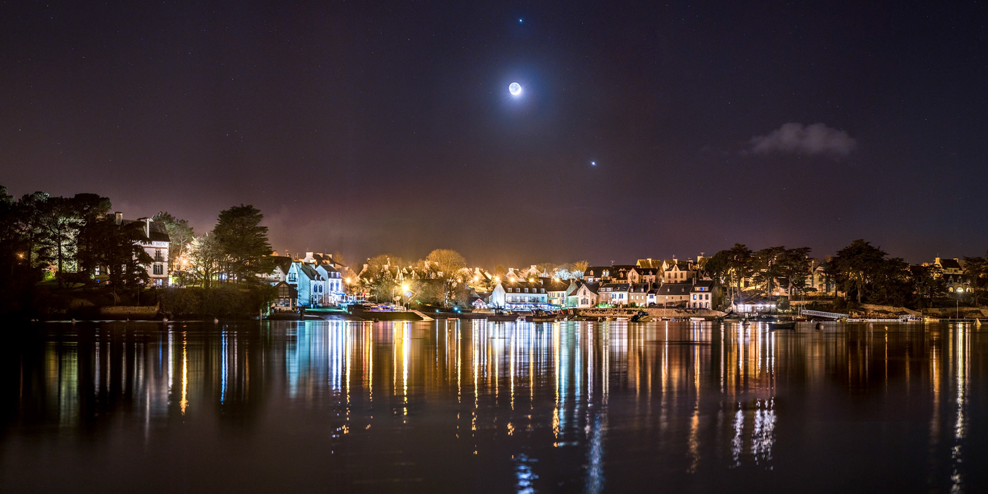 La puissante lumière orange des lampdaires du bourg de Sainte-Marine est difficile à équilibrer dans ce ciel tout noir. Heureusement que quelques éclairages à LEDs blanches confèrent une certaines neutralité aux bâtiments situés dans le port. Dans le ciel, la Lune en Croissant (parée de sa lumière cendrée) a rendez-vous avec Vénus (en bas à droite de la Lune) et Jupiter (à la verticale de Sélène)..