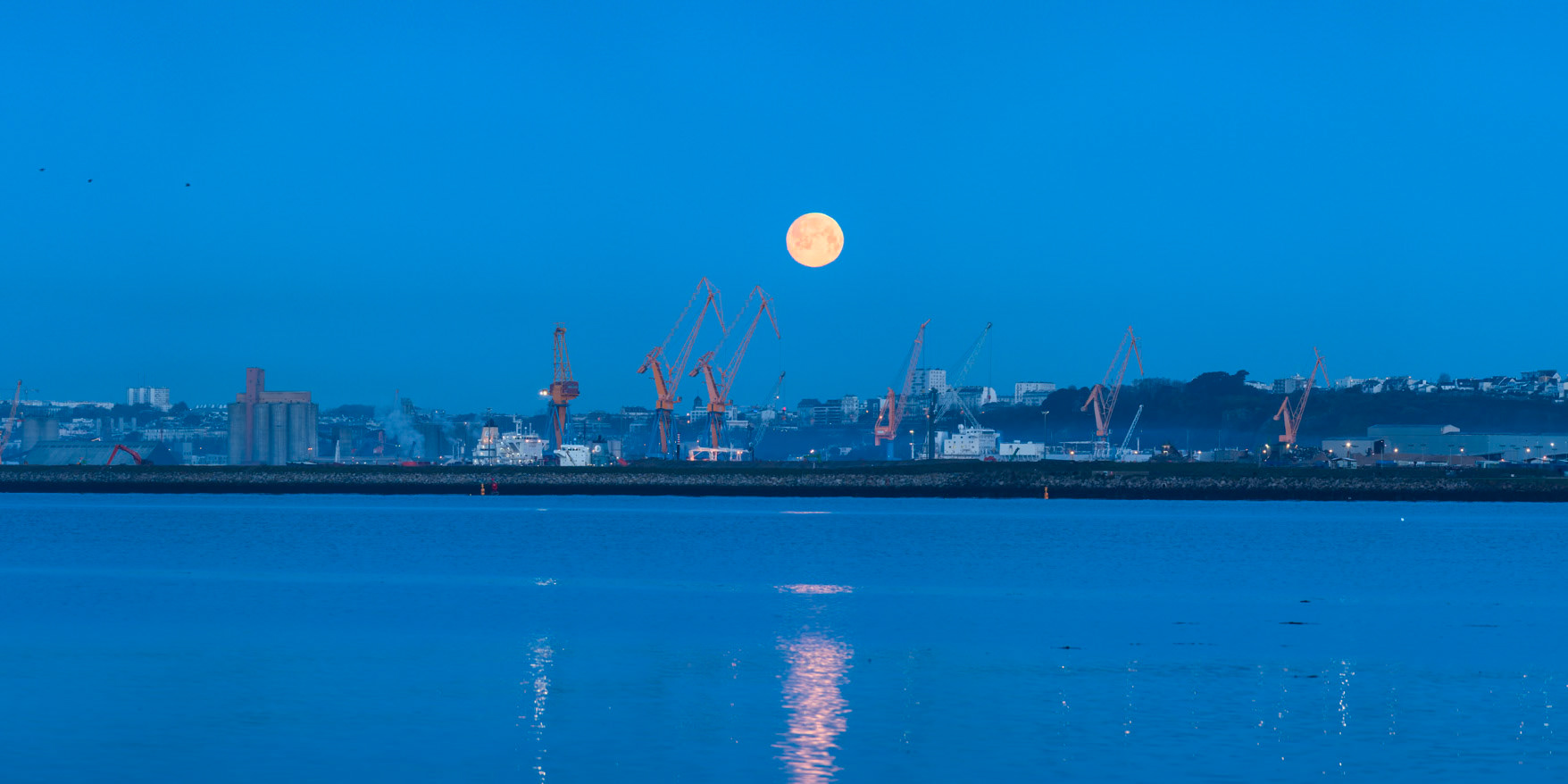 Un matin de mars, la Pleine Lune se couche derrière le port de commerce de Brest. Installé depuis Pors Keralliou, je profite du spectacle dans un ciel très clair.