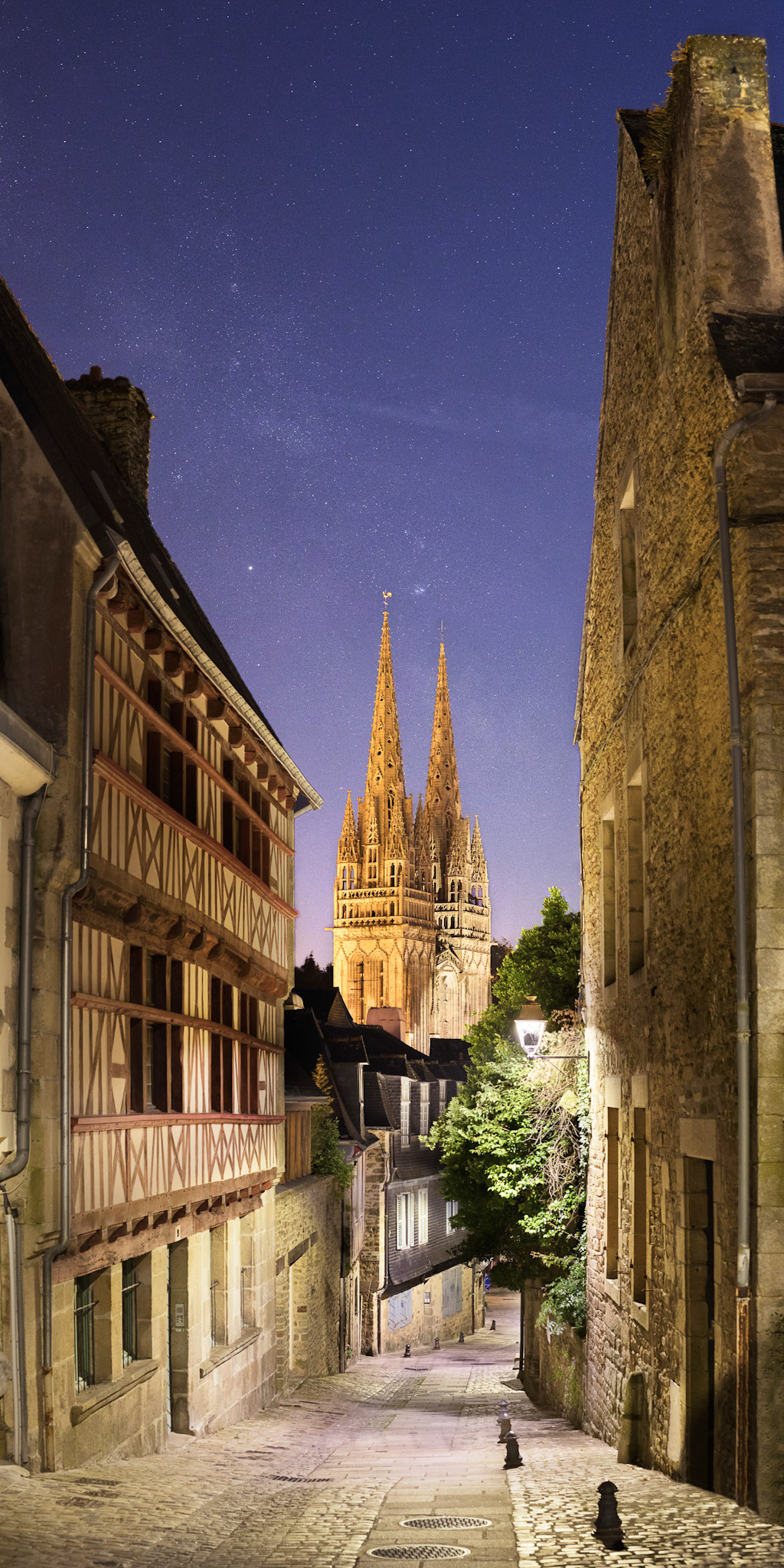 Depuis le haut de la rue du Lycée, la vue sur la cathédrale de Quimper est splendide. Les lampadaires bien conçus pour éclairer vers le bas permettent d'envisager de photographier la Voie lactée, malgré la présence de la Lune en Quartier qui teinte le ciel en bleu. J'ai dû composer différents temps de pose, de 1/15 s à 4 s pour capturer à la fois la rue éclairée et le ciel étoilé.