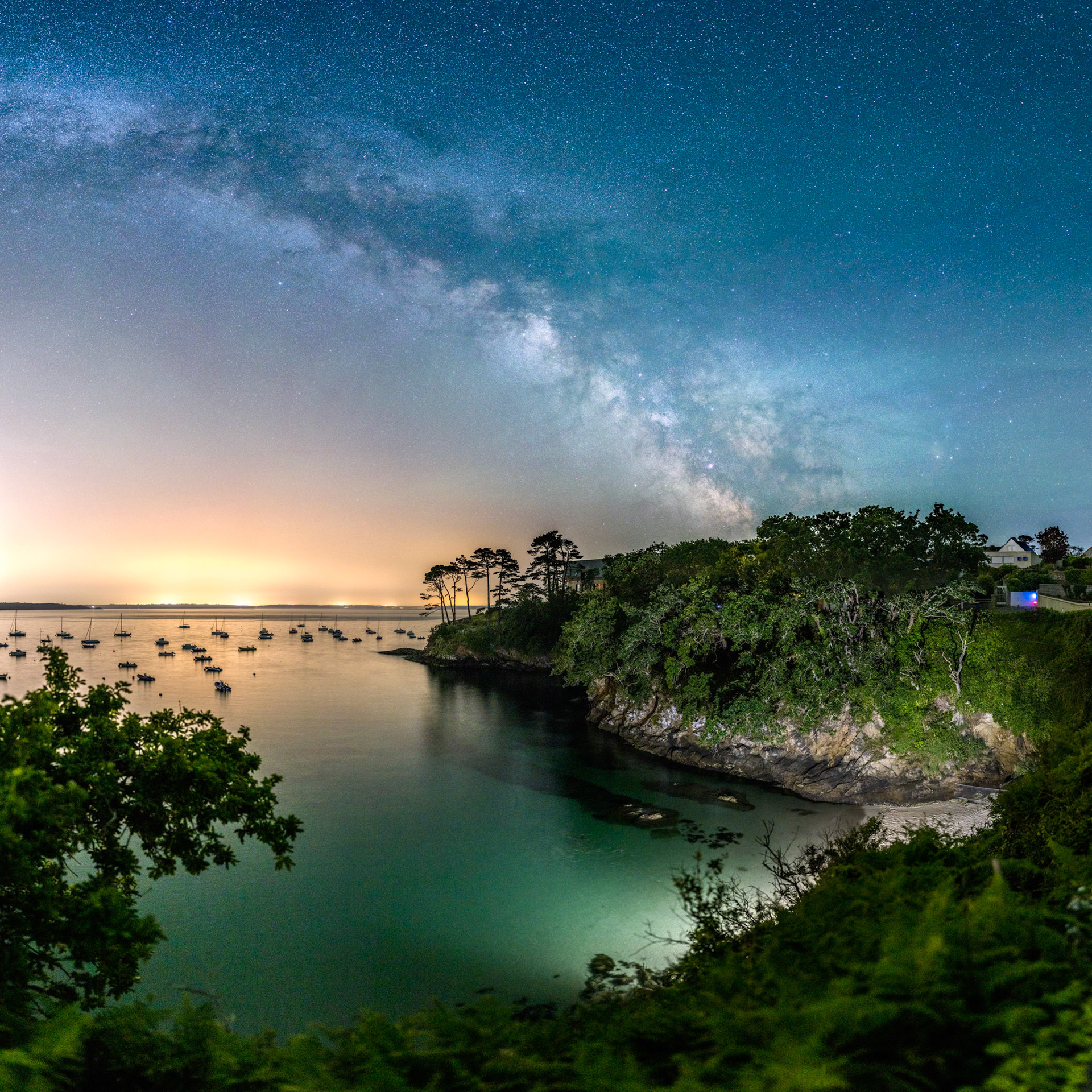 La Plage des Curés est un lieu assez discret mais d'une grande beauté. Le bouquet de pins au centre de la photo le caractérise, de même que la bande de rochers sombre immergés à marée haute. Mais comme le site est sombre, j'ai été déposer mon smartphone avec son flash allumé au pied des escaliers afin d'illuminer la mer et la petite falaise. Au fond à gauche, le halo orange de pollution lumineuse de l'Île Longue réchauffe bien la photo.