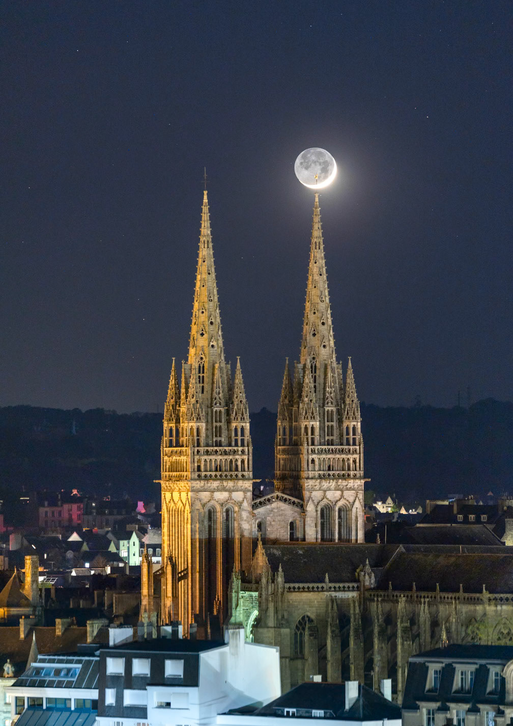 Le Croissant de Lune (complété par sa lumière cendrée) se lient au bout d'une des flèches de la cahtédrale Saint-Corentin. La silhouette de le girouette qui orne son sommet se dessine sur fon de Lune.
