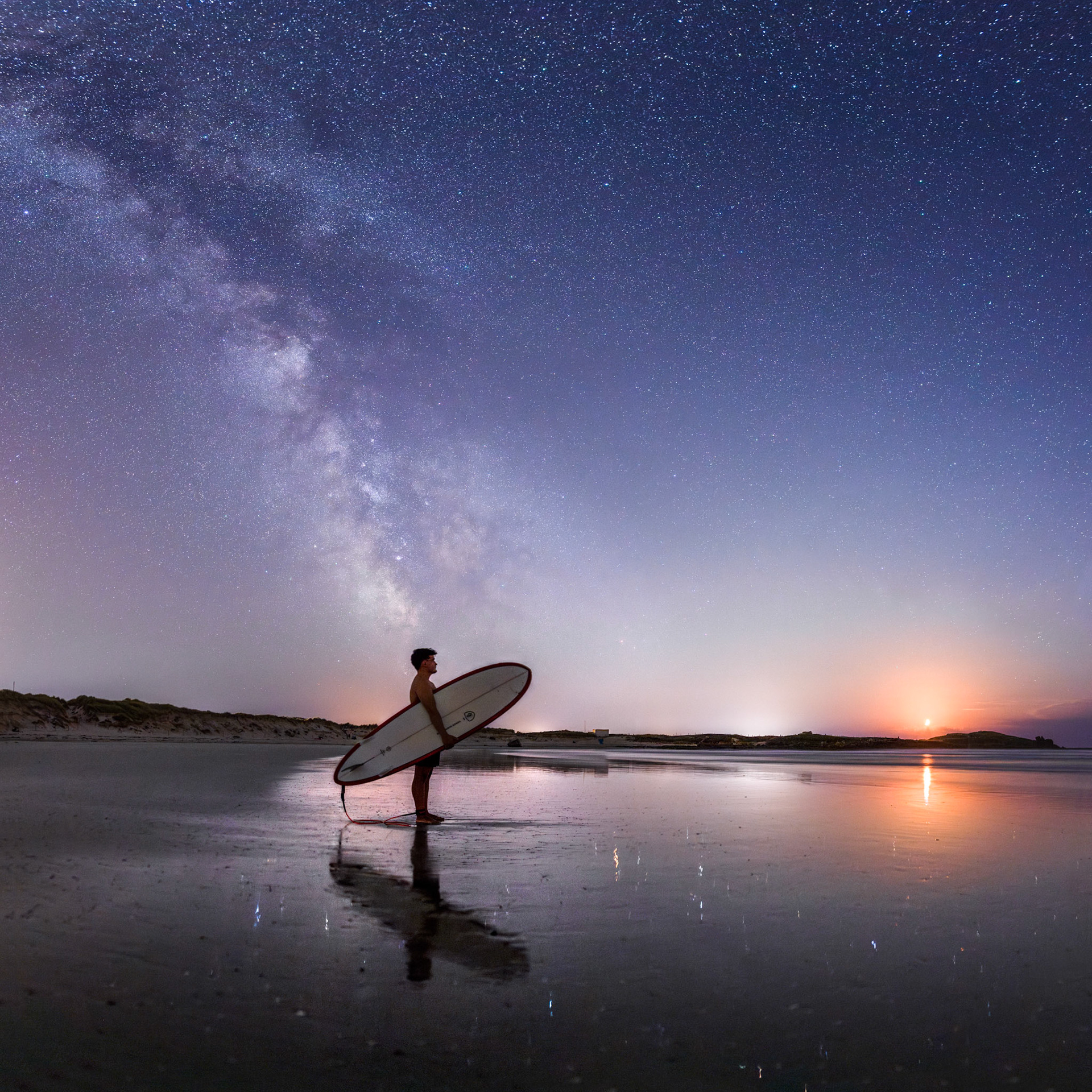 Mon neveu Enzo se tient face à l'océan sur la plage de La Torche. Sa silhouette se reflette sur le sable mouillé. La Voie lactée émerge derrière lui tandis qu'il contemple le Quartier de Lune qui se dresse au-dessus de la Pointe de La Torche.