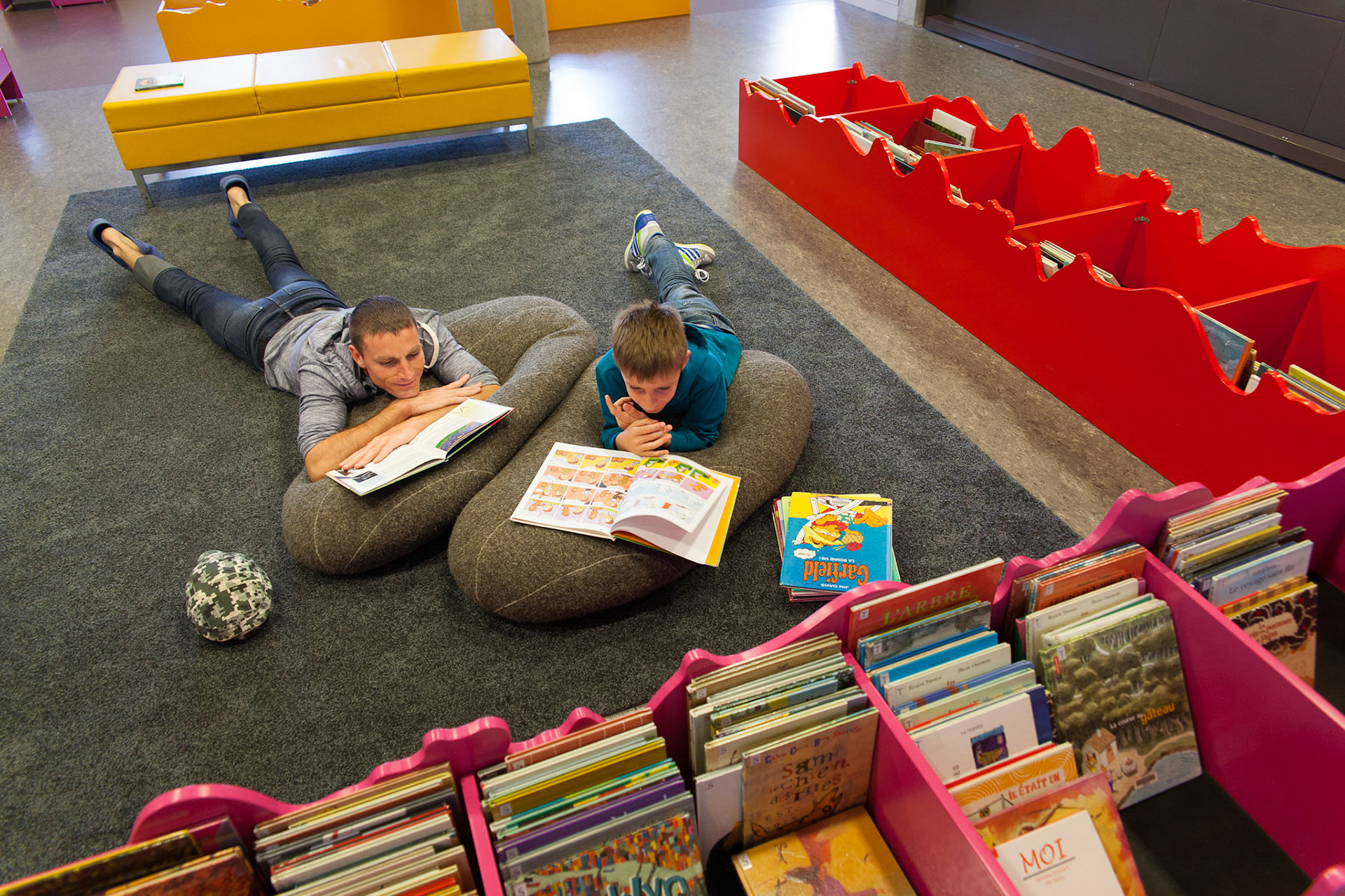 Un père et son fils sont confortablement installés dans l'espace jeunesse de la médiathèque des Ursulines.