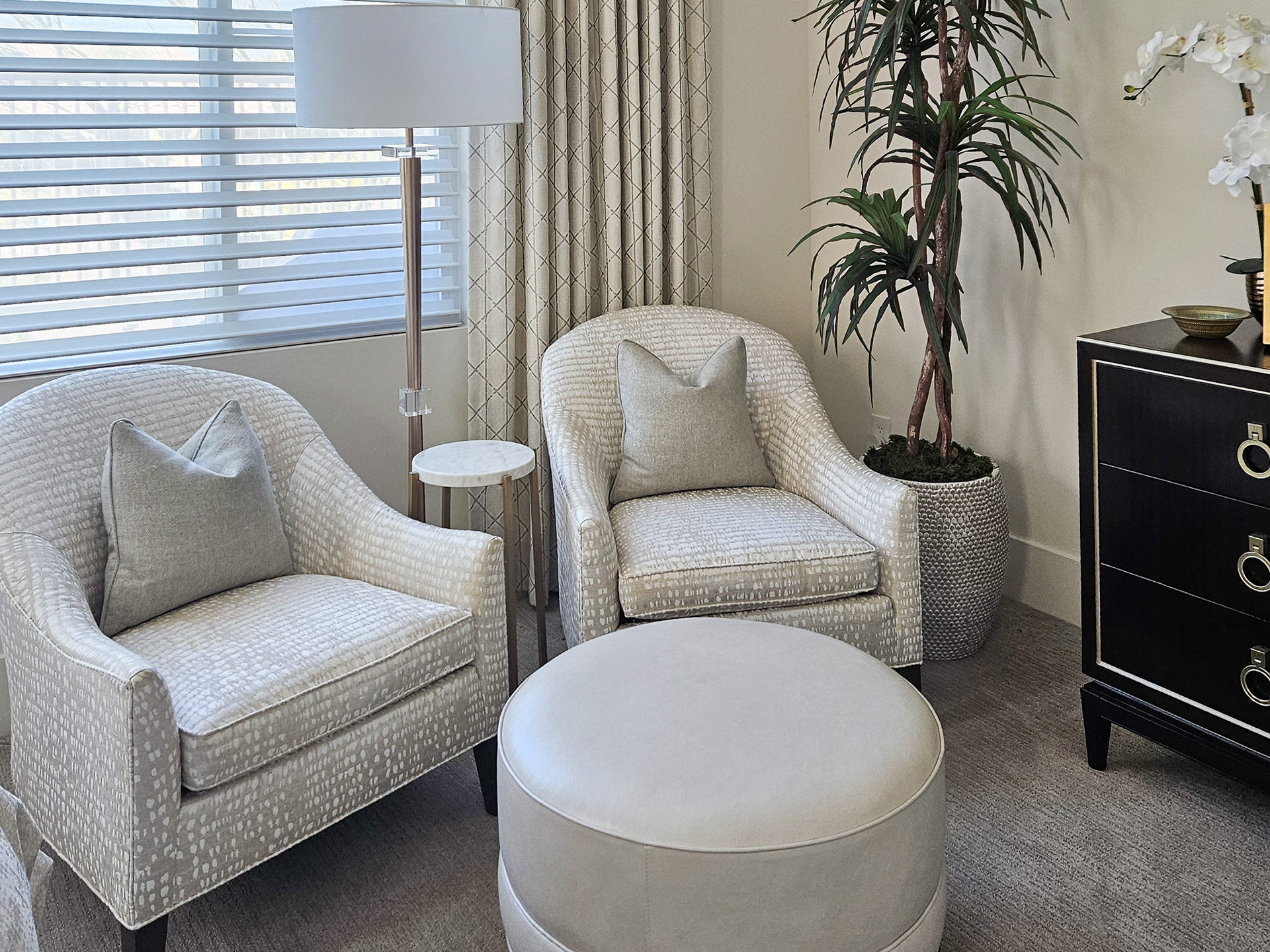 A tailored arrangement of patterned club chairs and shimmering textiles, grounded by the architectural weight of a black and gold chest.