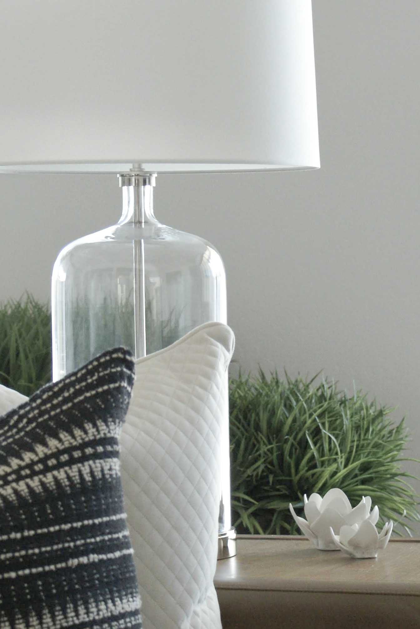 Close-up detail of curated residential interior styling by Elizabeth Brown in Panama City, Florida, featuring biophilic greenery, a glass table lamp, textured pillows, and decorative ceramic lotus flowers.