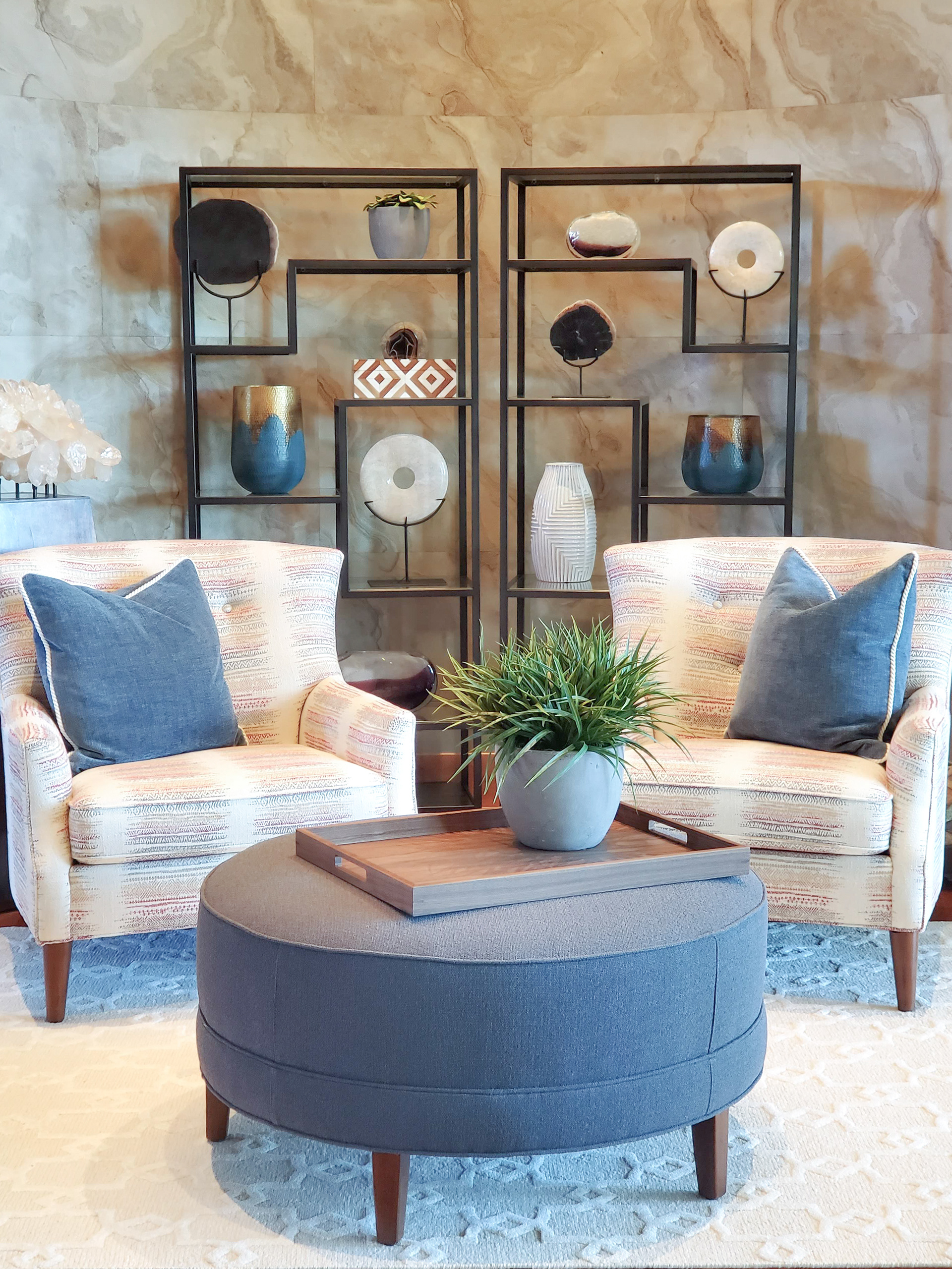 A professionally styled living room featuring custom upholstered armchairs, a blue velvet ottoman, and curated built-in shelving, showcasing the final result of the Elizabeth Brown design process.