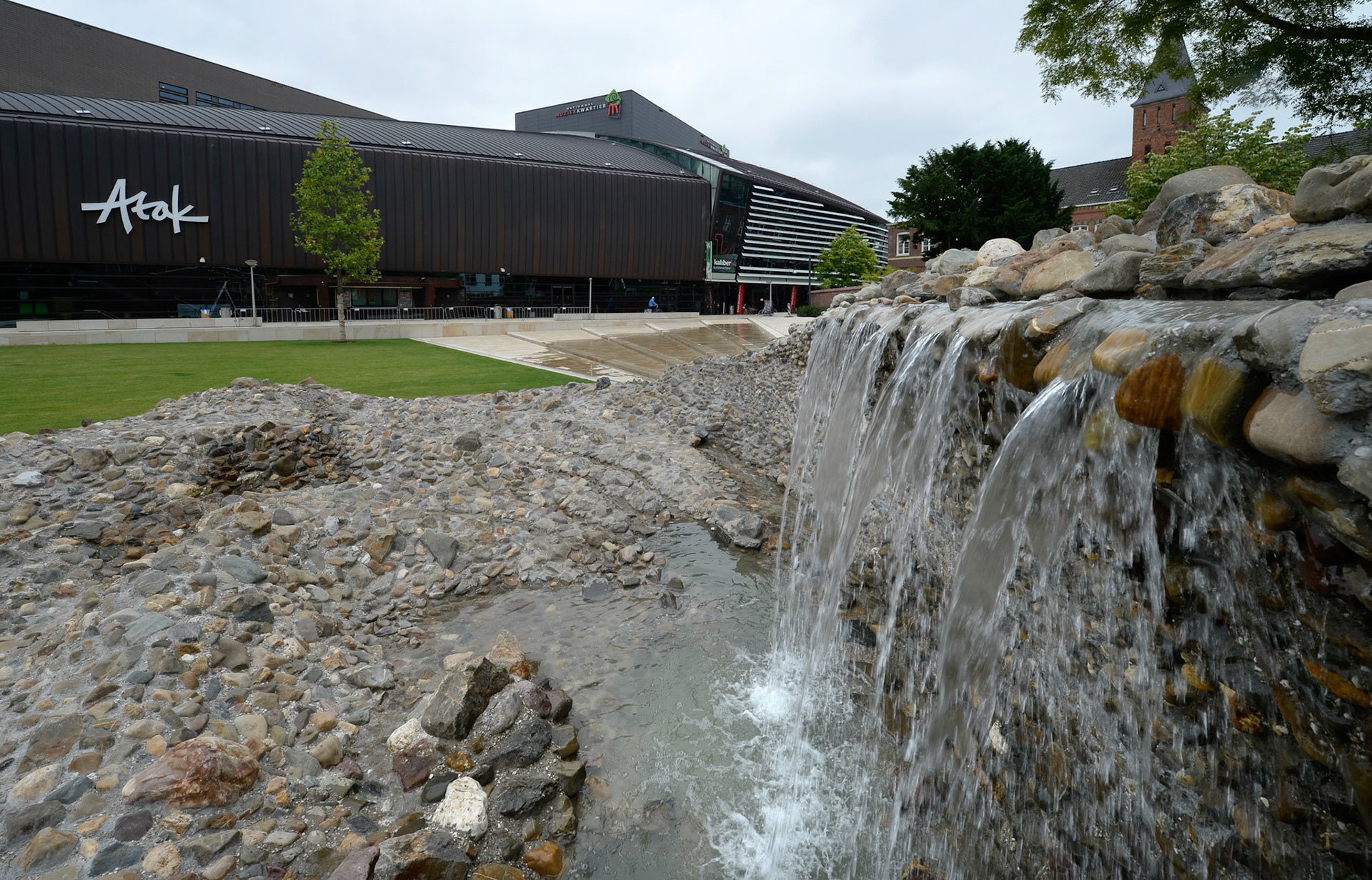 NIEUWE STADSTUIN VOOR ENSCHEDEWoensdag 18 juni zette wethouder Hatenboer de kraan open van het kunstwerk Vortex, onderdeel van het nieuwe Willem Wilminkplein in het centrum van Enschede. Sindsdien stroomt het water over een brede, luie natuurstenen trap richting de Vortex. Het kunstwerk is een uit keien opgebouwde ÔdraaikolkÕ waarin een waterval over een muurtje drie meter omlaag klatert.Kunstenaar Jeroen Doorenweerd ontwierp in nauwe samenwerking met gemeentelijk ontwerper Hans Schršder deze eigentijdse folly als integraal onderdeel van de trap en het plein. Hiermee heeft Enschede een sfeervolle groene huiskamer erbij gekregen.Komende zomermaanden kan het publiek het plein en het kunstwerk testen op hun recreatieve kwaliteiten. Op vrijdag 19 september vindt vervolgens de offici‘le opening van het plein plaats met een feestelijke act als startsein van het Willem Wilminkfestival.Muziekkwartier met Willem WilminkpleinIn het Muziekkwartier van Enschede zijn alle belangrijke muziekpodia- en gezelschappen van de stad te vinden. In het hart ervan ligt het nieuwe driehoekige Willem Wilminkplein. Historische gebouwen zoals een voormalig klooster en een fabrieksschool begrenzen samen met nieuwe gebouwen het plein en verlenen het karakter en intimiteit. Het Wilminktheater (2008) van Ector Hoogstad Architecten vormt met het nog op te leveren hotel van Dick van Gameren ŽŽn lange wand. Aan de overzijde realiseerde Onix architecten dit jaar een appartementencomplex met winkels en horeca.Het plein zal een oase in de stad zijn; slechts toegankelijk voor voetgangers en fietsers. Het grote grasveld, de banken eromheen en de cafŽterrassen nodigen uit om de ruimte als stadstuin te gebruiken. Aanlokkelijk middelpunt aan de oostkant vormt de waaiervormige luie trap waar water overheen stroomt, uitmondend in het kunstwerk Vortex. De trap kan gebruikt worden als podium voor kleinschalige muziekoptredens. Een andere blikvanger aan de westkant van het plein wordt de nog in aanbouw zijnde monumentale buitentrap die toegang zal geven tot de muziekschool in het Wilminktheater en het nieuwe hotel. Ook deze trap kan als podium en verblijfsplek dienen en biedt bovendien uitzicht op het naastgelegen stationsplein.VortexDe vorm van het plein inspireerde kunstenaar Jeroen Doorenweerd (Tilburg) tot zijn kunstwerk. Hij vertelt: ÒHet plein is driehoekig en door de diagonalen krijgt de ruimte dynamiek. De treden van de trap zijn samengeknepen lijnen die op het smalste punt een natuurlijke aanleiding vormen voor een cirkel, waarin de Vortex ligt. Over een wandje klatert water drie meter omlaag als een gecultiveerde waterval. Via stapstenen kun je, als je durft, naar beneden lopen, achter het water langs. De vormgeving met keien is afgeleid van de techniek van de gewassen grindtegel, die in de jaren zeventig grote populariteit genoot.ÓDoorenweerd over de inhoud van zijn werk: ÓVortex betekent eigenlijk werveling, in vloeistof of in lucht, zoals een draaikolk of een tornado. Daarnaast is het ook een term die veel in de Science Fiction wordt gebruikt; Ôto disappear into the vortexÕ wil zeggen dat je in een andere tijd en ruimte terecht komt. Je wordt tegen wil en dank meegenomen naar een andere wereld en daar ligt een parallel met kunst, want kunst behoort dat eigenlijk ook te doen.Ó©foto eric brinkhorst