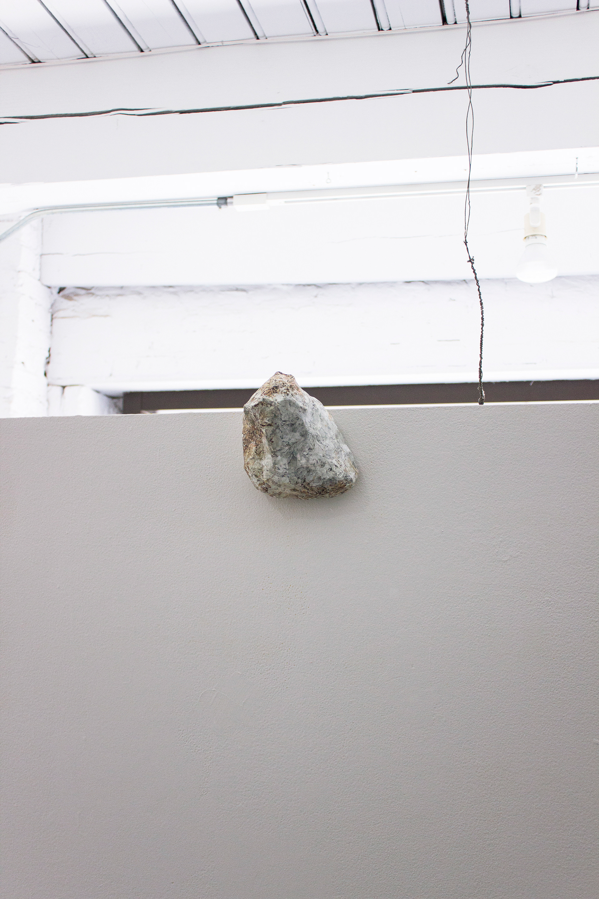 "Their Natural State" Rubble sculpture hangs at the top center edge of the gallery's freestanding wall.
