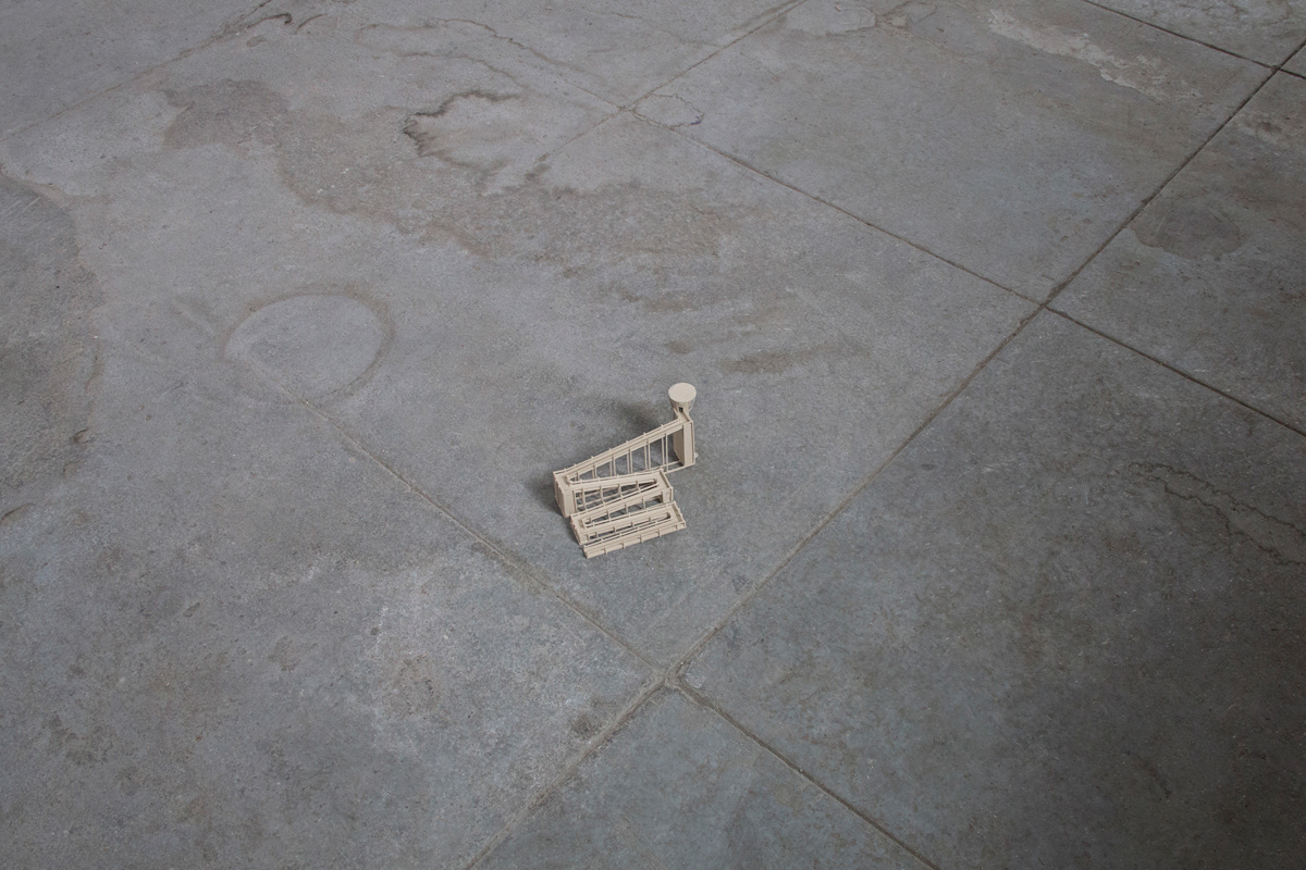 bird-eye view of a small balsa wood model of a watchtower on top of a concrete floor. It has a long accessibility ramp reaching to the top.