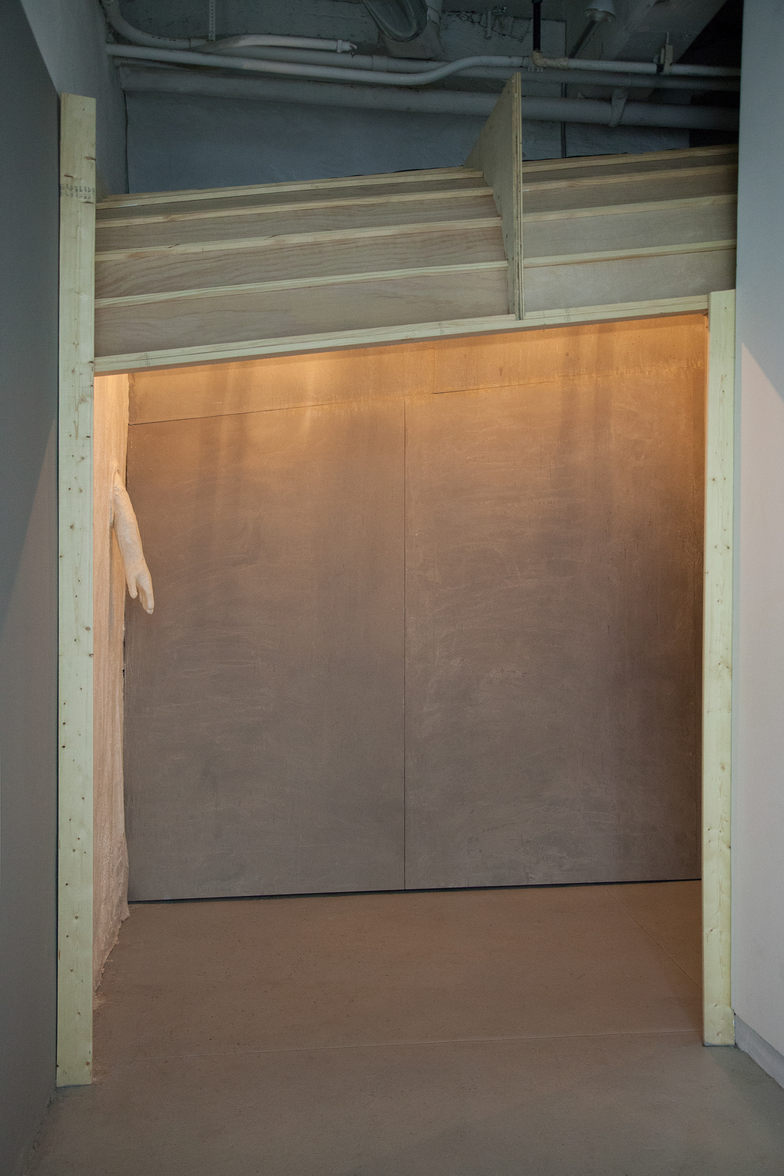 View of the tunnel-like structure once walking through into the gallery and looking back. From this view you can see the exterior wooden panel construction of the installation.