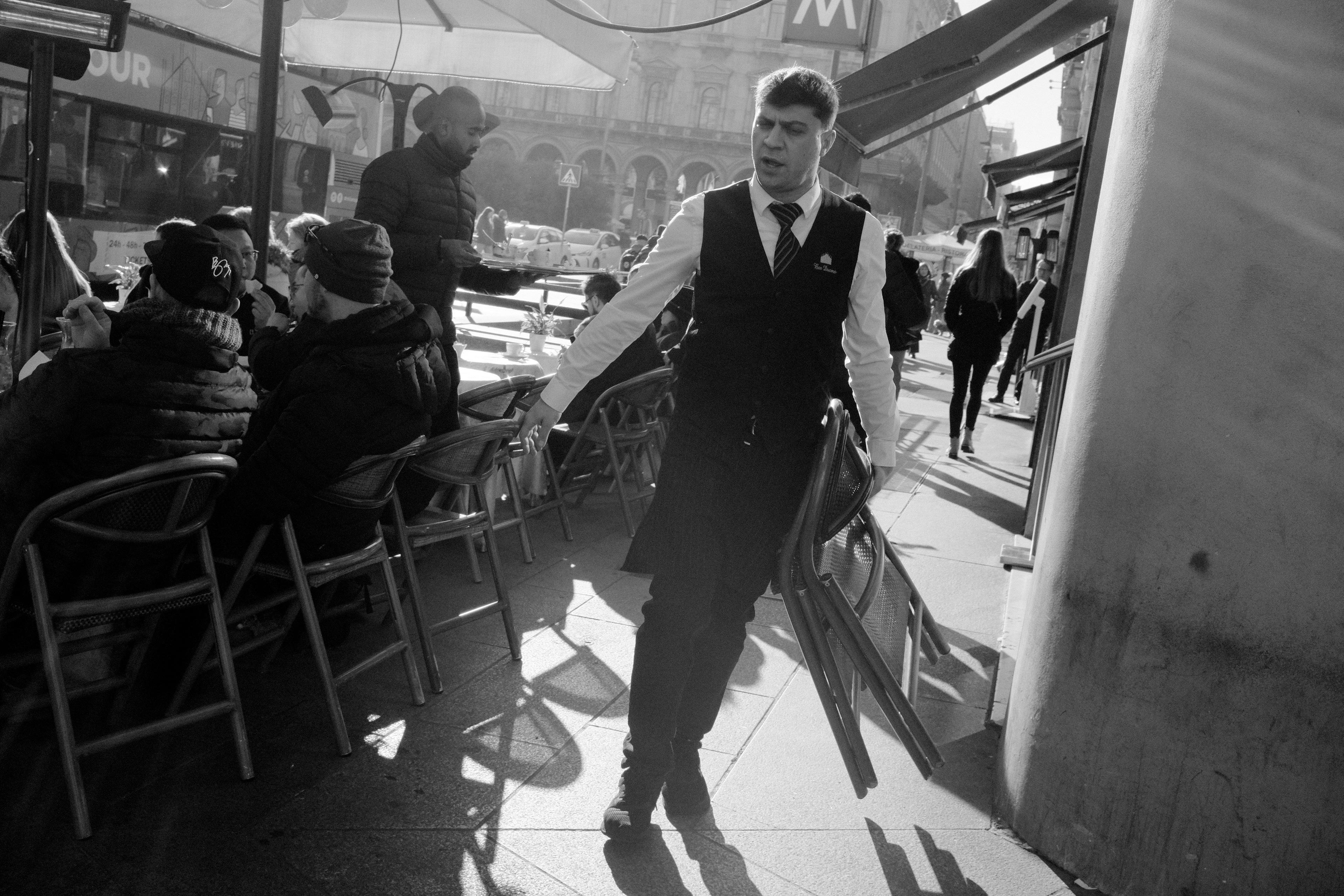 Waiter carrying chairs. Milan, Italy 2025.
