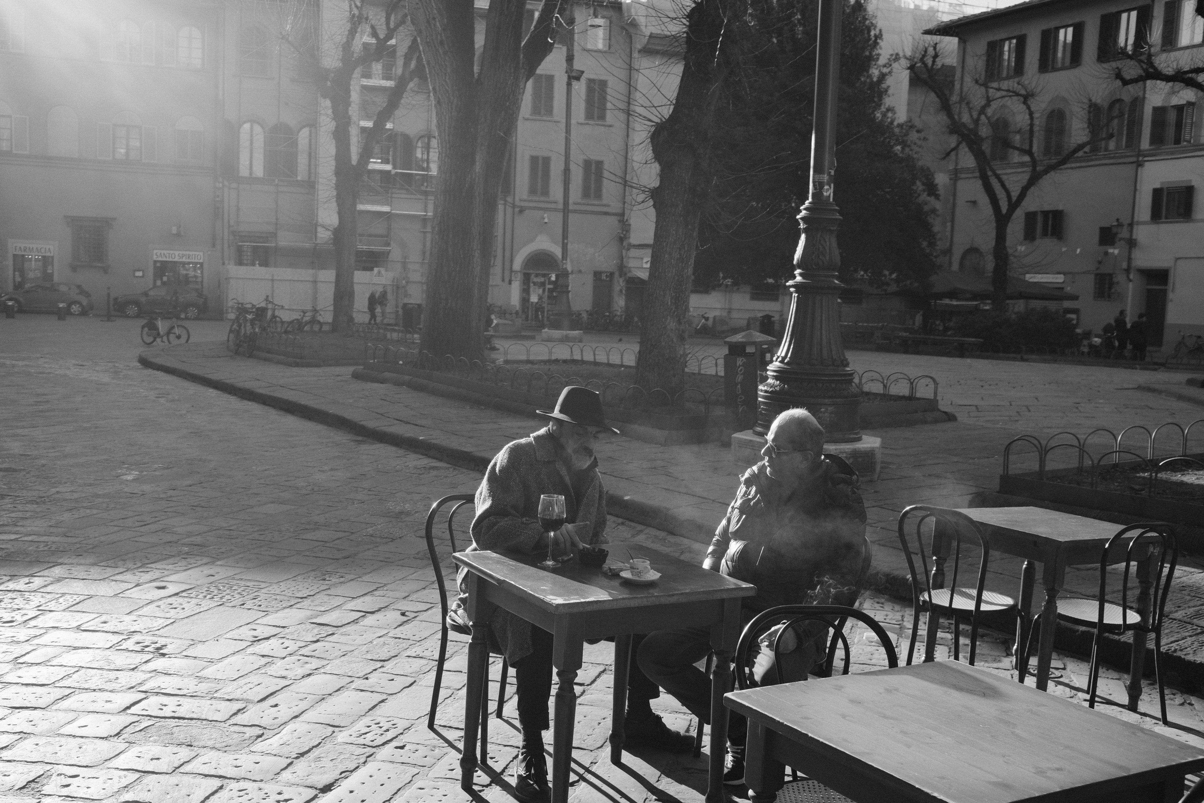 Two men in the midst of a conversation drinking and smoking. Florence, Italy 2024.