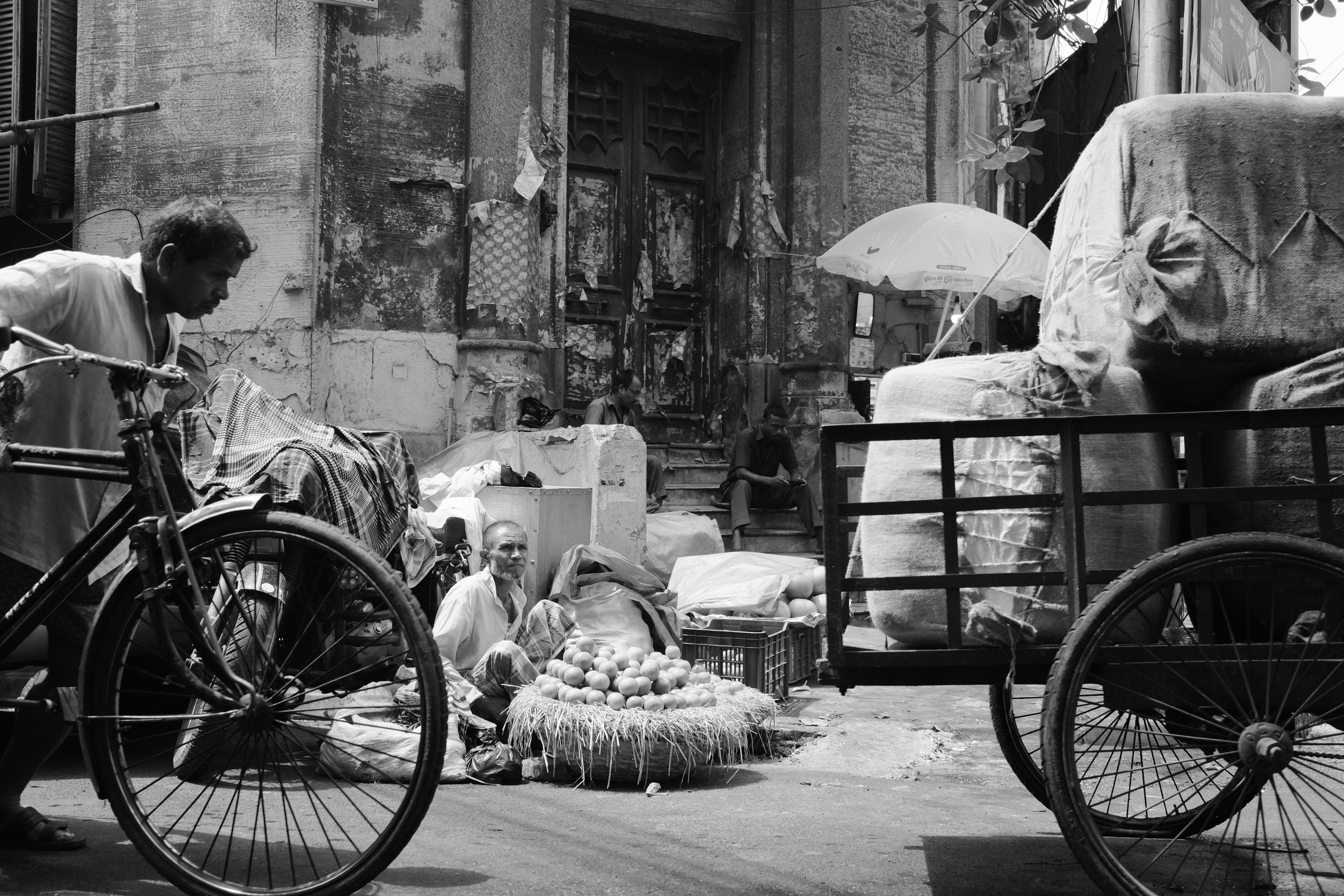 Hawker selling fruits in the street with cycle rickshaw pullers in the foreground. Calcutta, India 2024.