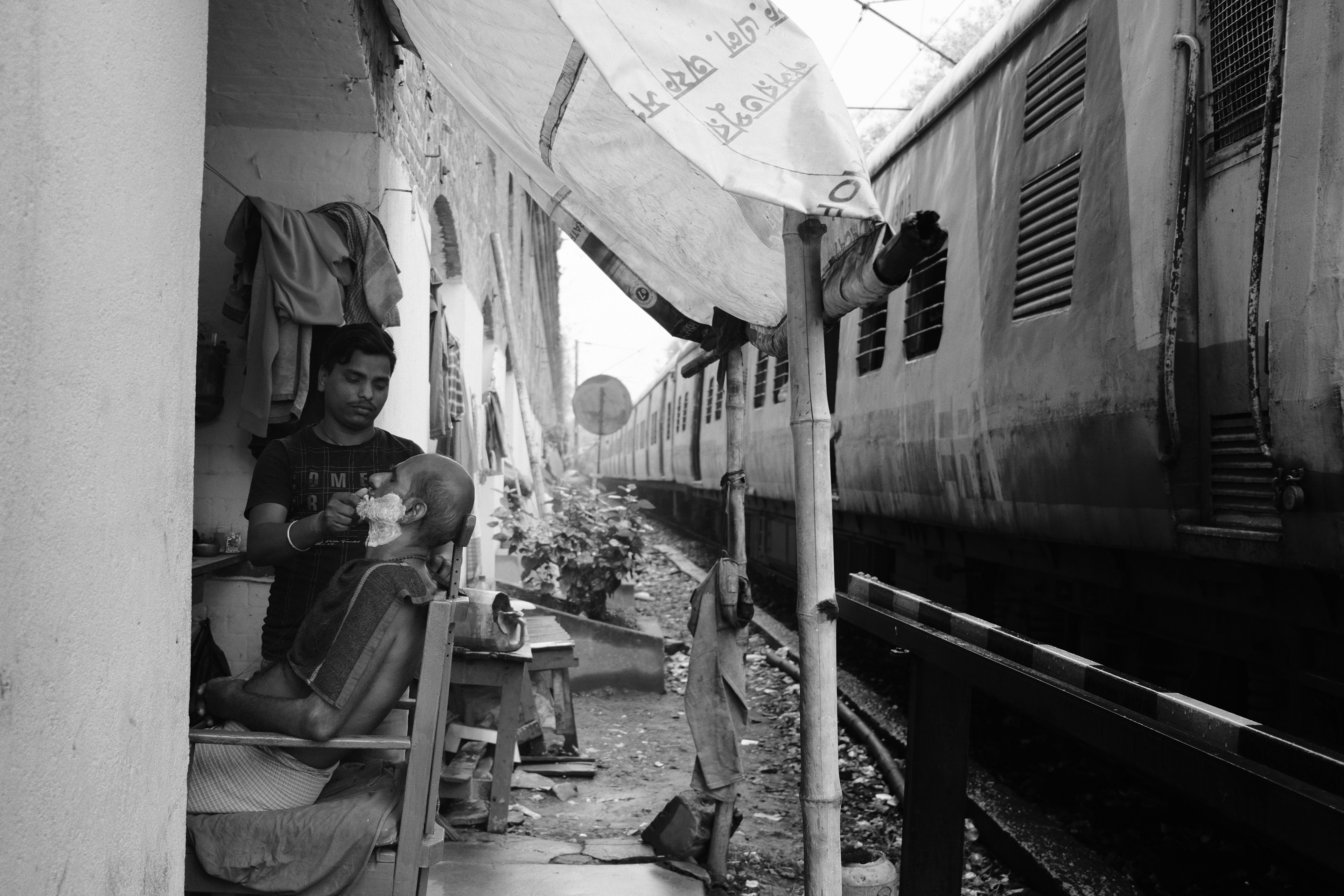 A barber working next to a passing train. Calcutta, India 2024.