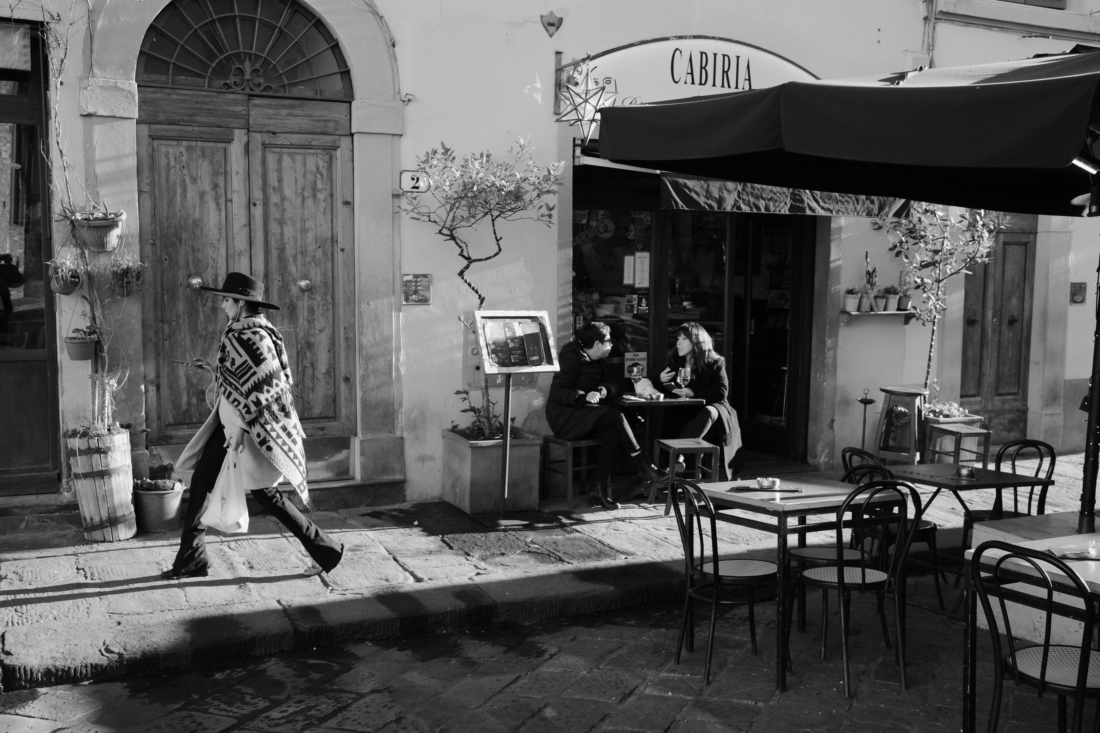 Two women at a café and another passing by. Florence, Italy 2024.