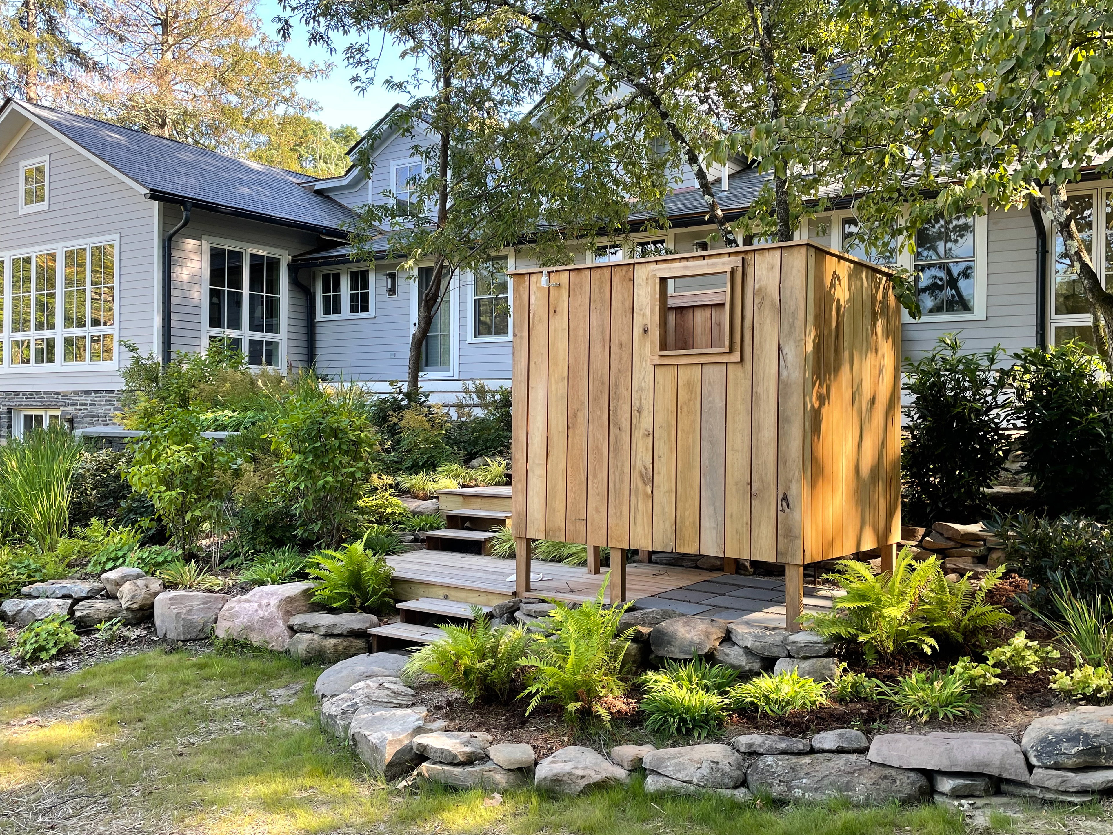 An outdoor shower in the rear of the home nestled within terrace plantings