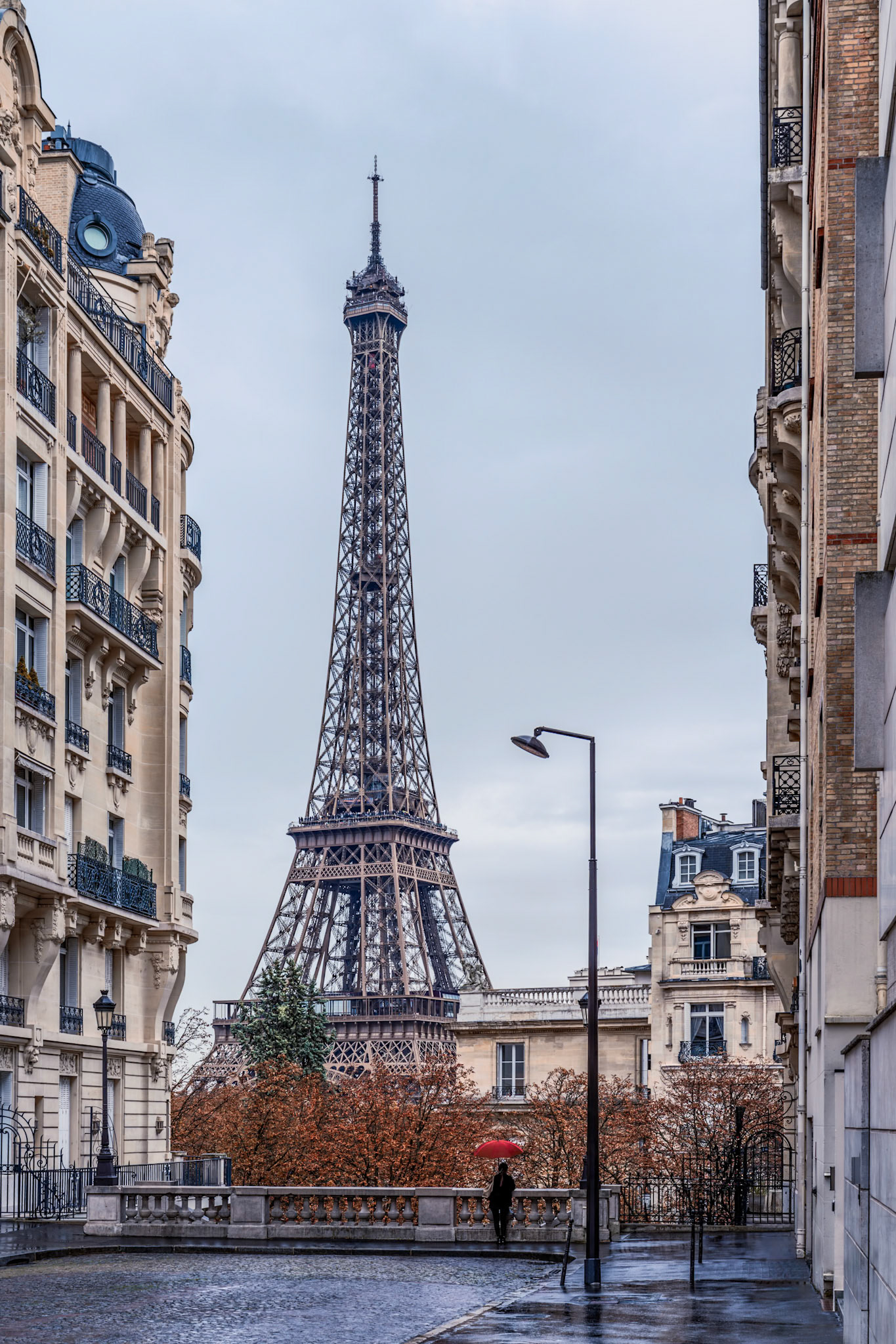 A Parisienne out for a stroll on a rainy, autumn afternoon pauses to admire the magnificent Eiffel Tower looming large in the distance.
