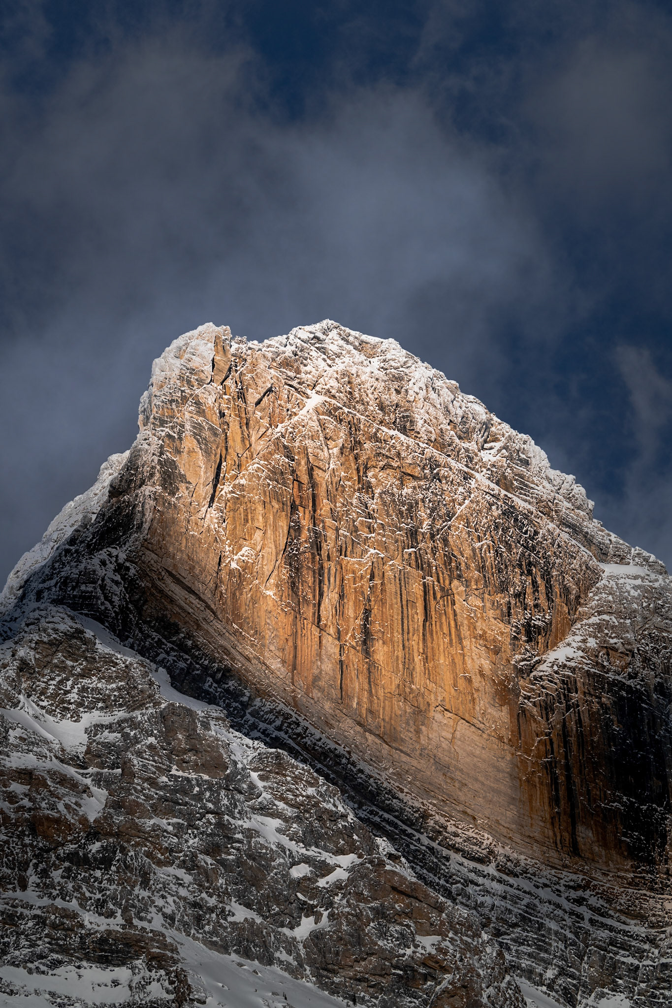 Golden light briefly kisses a mountain peak in the Alberta Rockies as the sun passes in and out of the clouds.