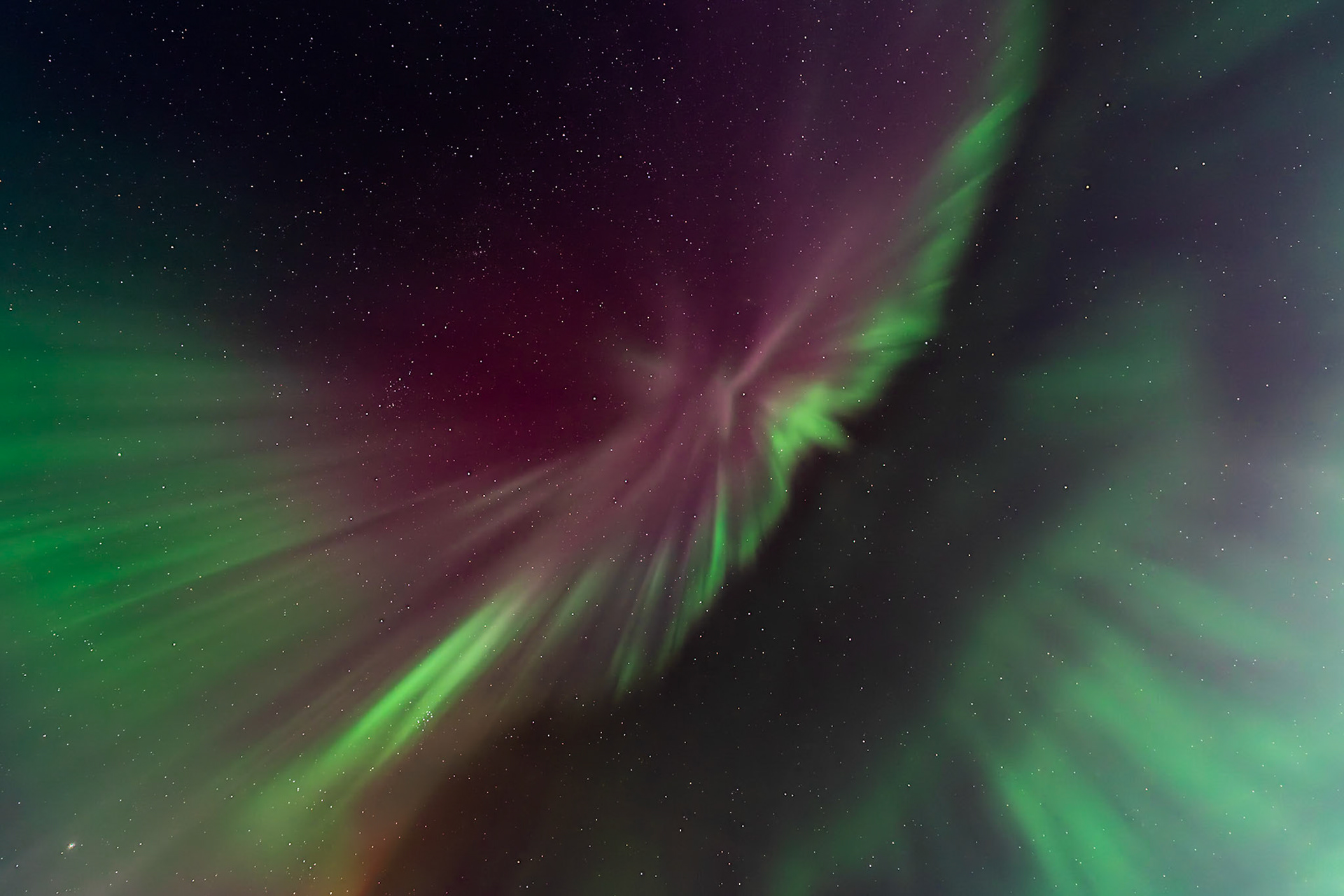 An auroral firebird born of red and green light spreads its wings and glides through the night sky.