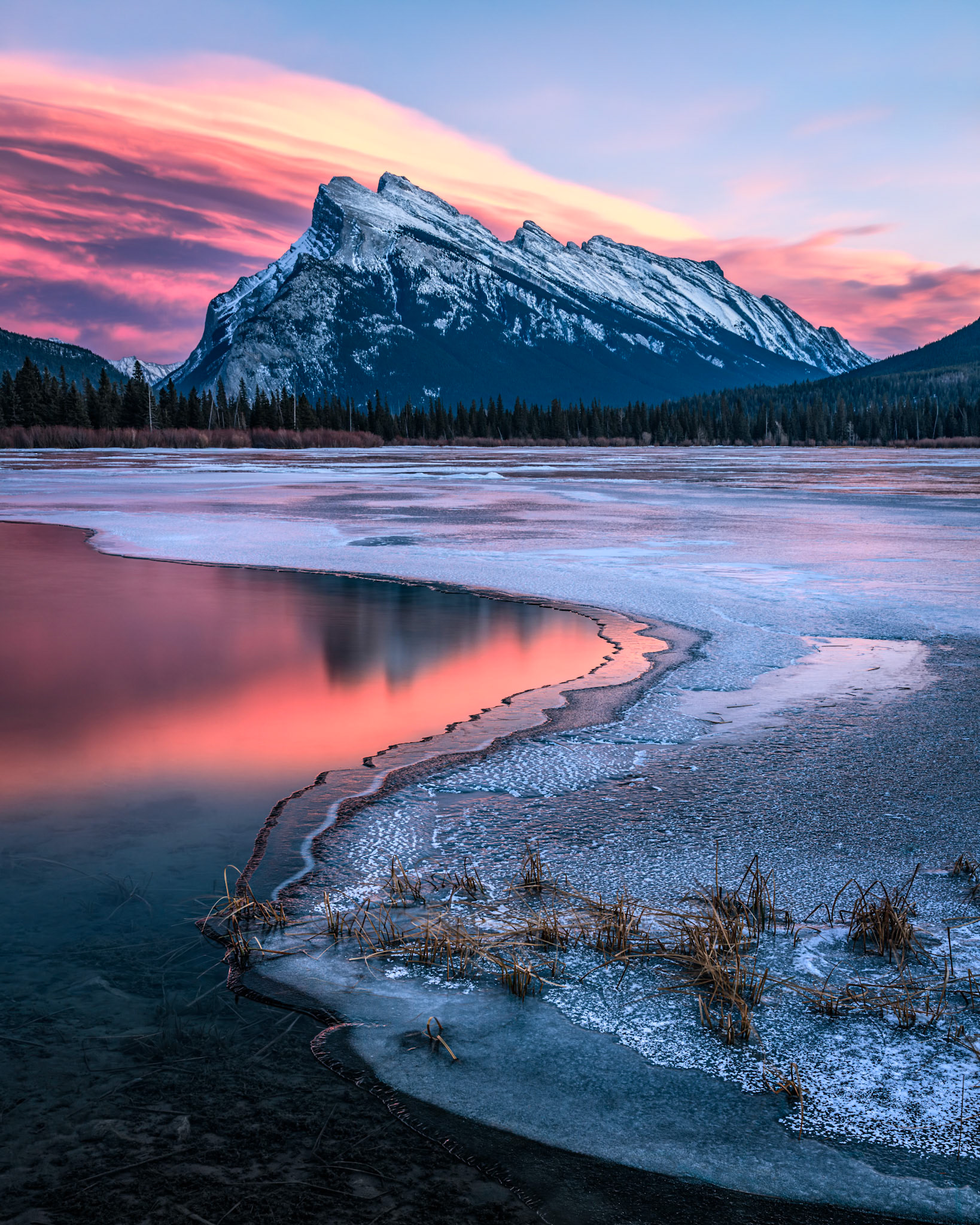 The setting sun ignites the clouds while the water and ice reflect the spectacular colour, in Banff National Park.