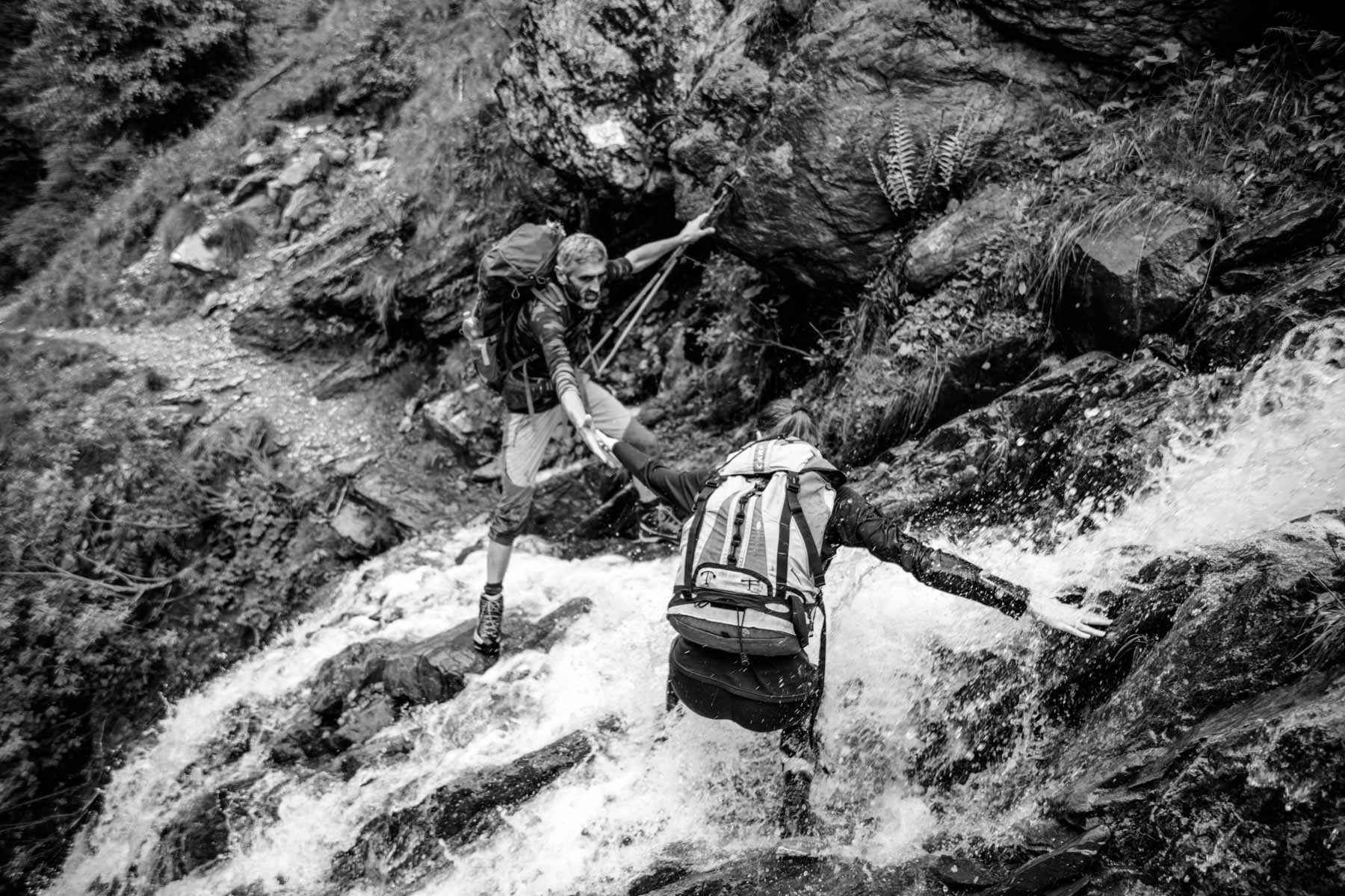 The hut owner helping one employee to cross a waterfall