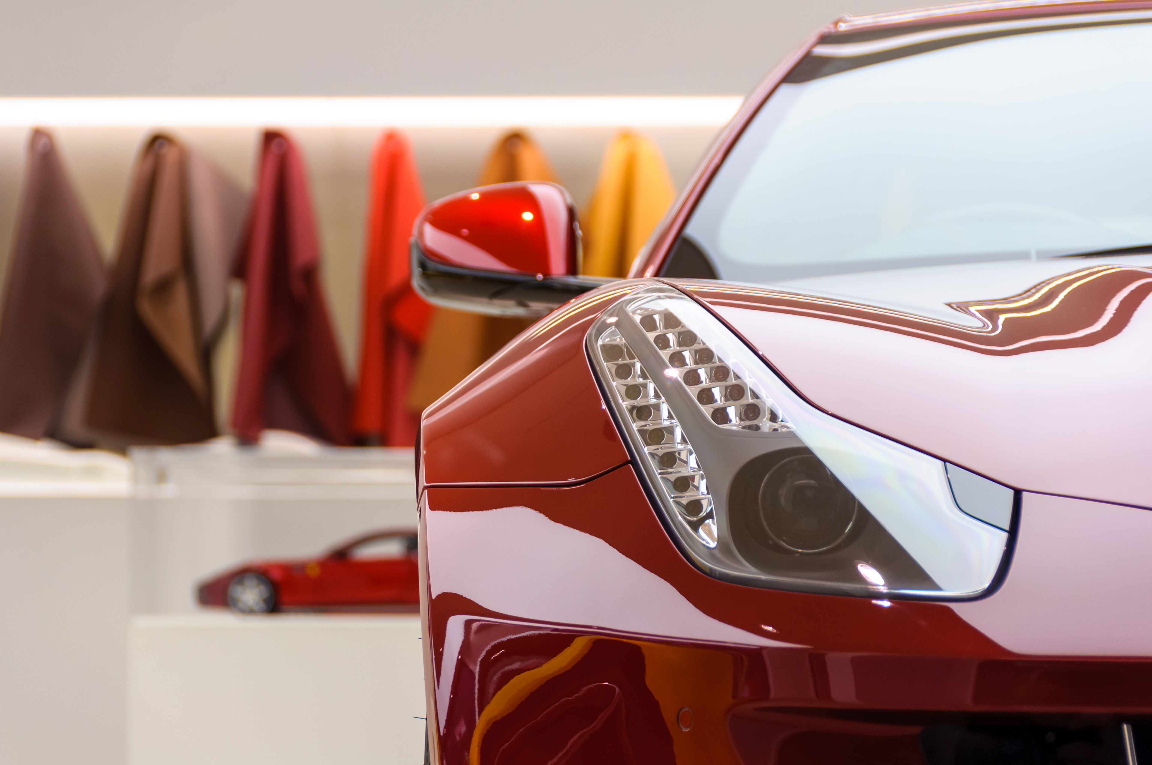 Red Ferrari FF on display in a showroom, leather samples in the background.