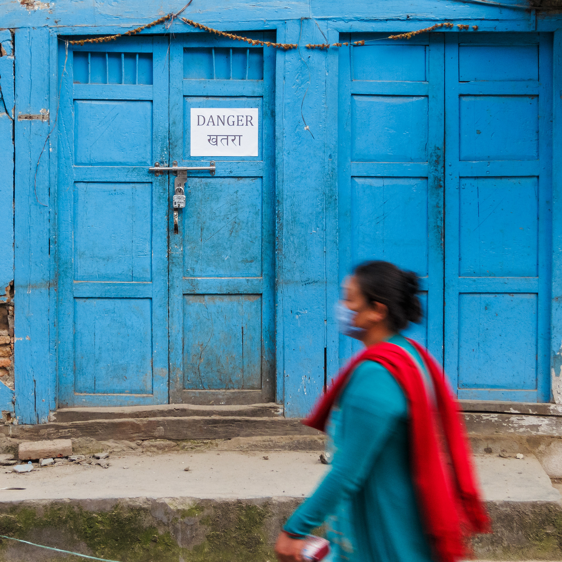 Kathmandu, Nepal - May 11, 2015: A woman walks past a danger sign on an old traditional house in Handigaun. The house was rendered dangerous by the 25 April Nepal earthquake.