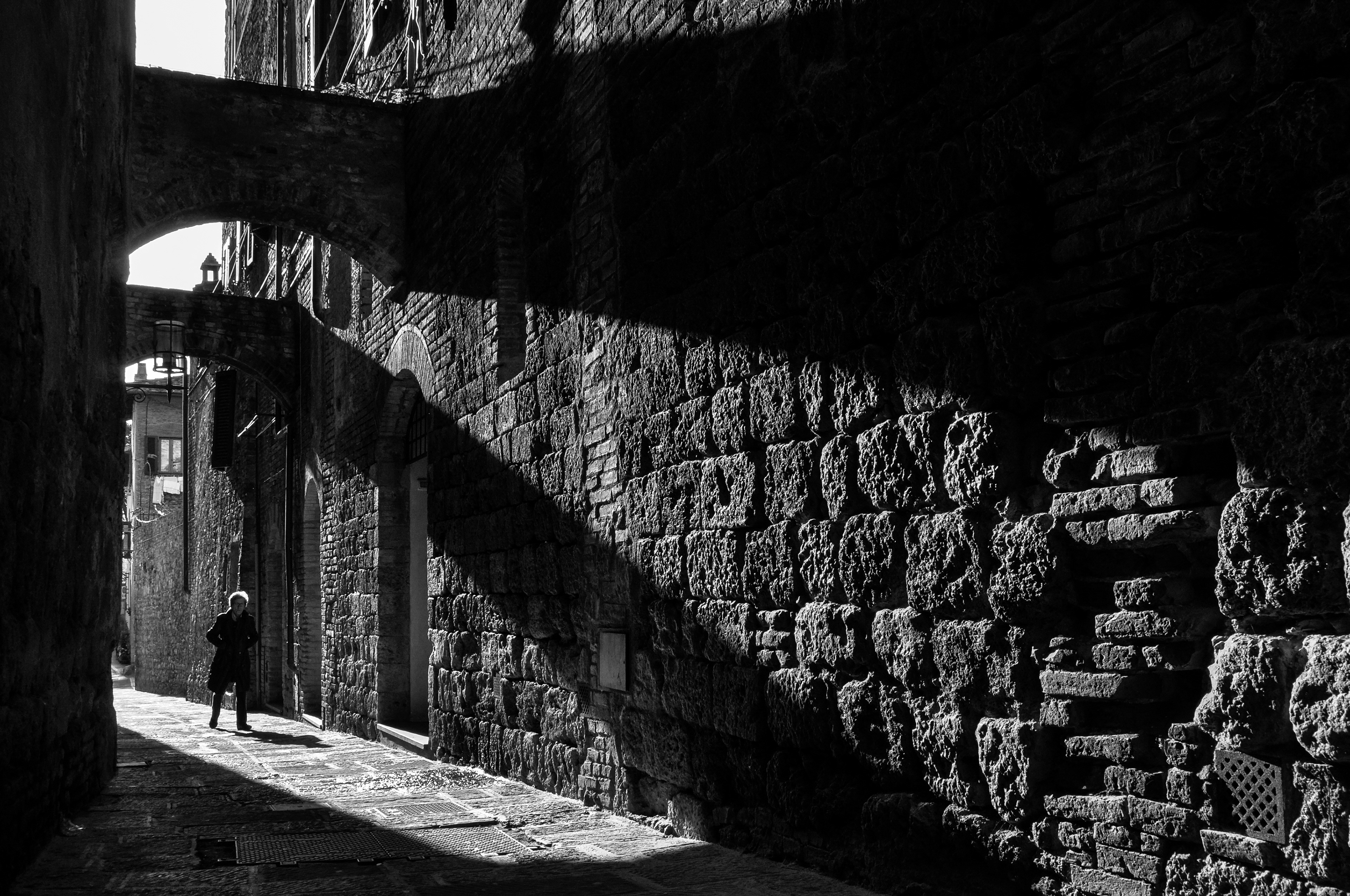 A pedestrian in a narrow medieval street in San Gimignano, Tuscany, Italy. Black and white photo.