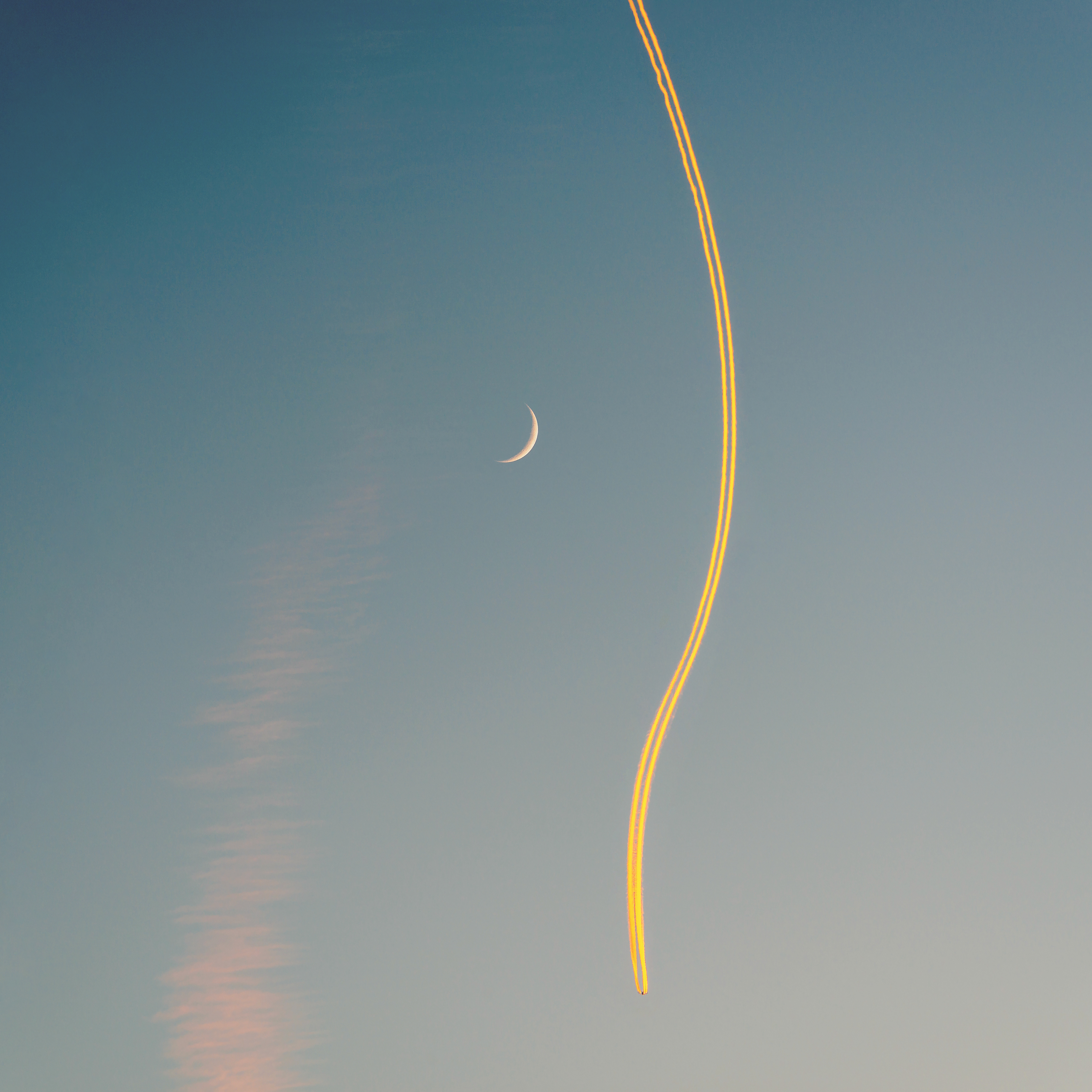 Jet airplane, its contrail and a crescent moon at sunset