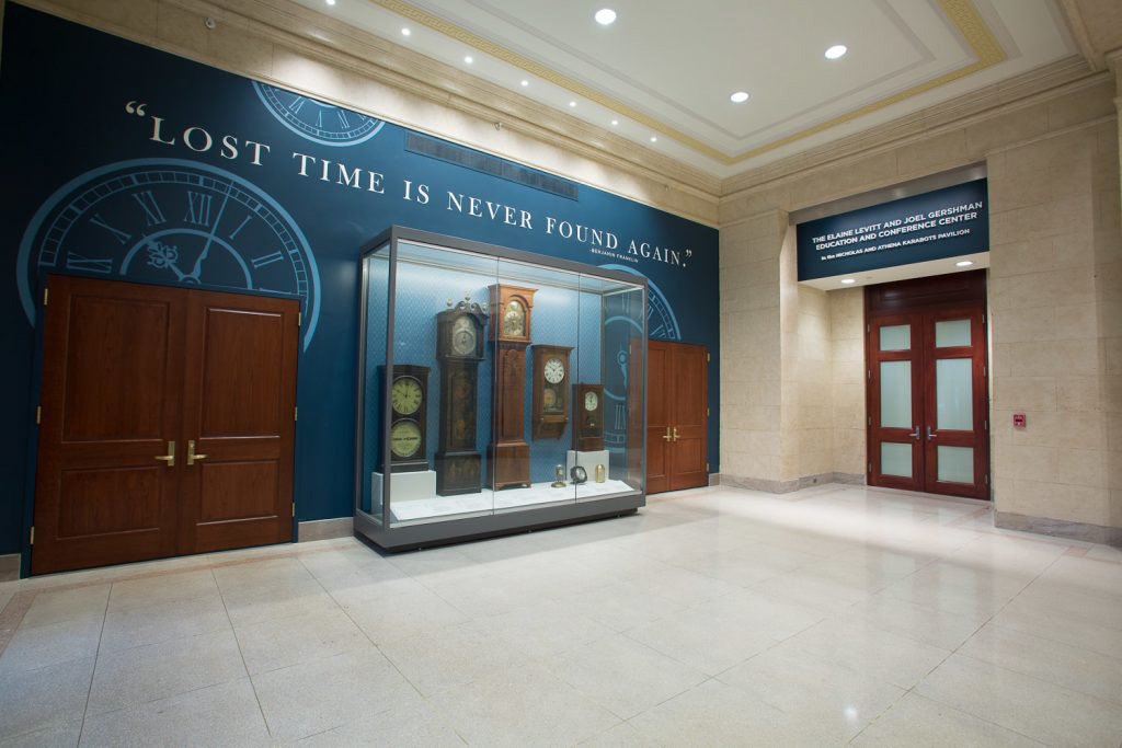 Full view of the clock collection, showing the mural wall, display case, and matching wayfinding signage.