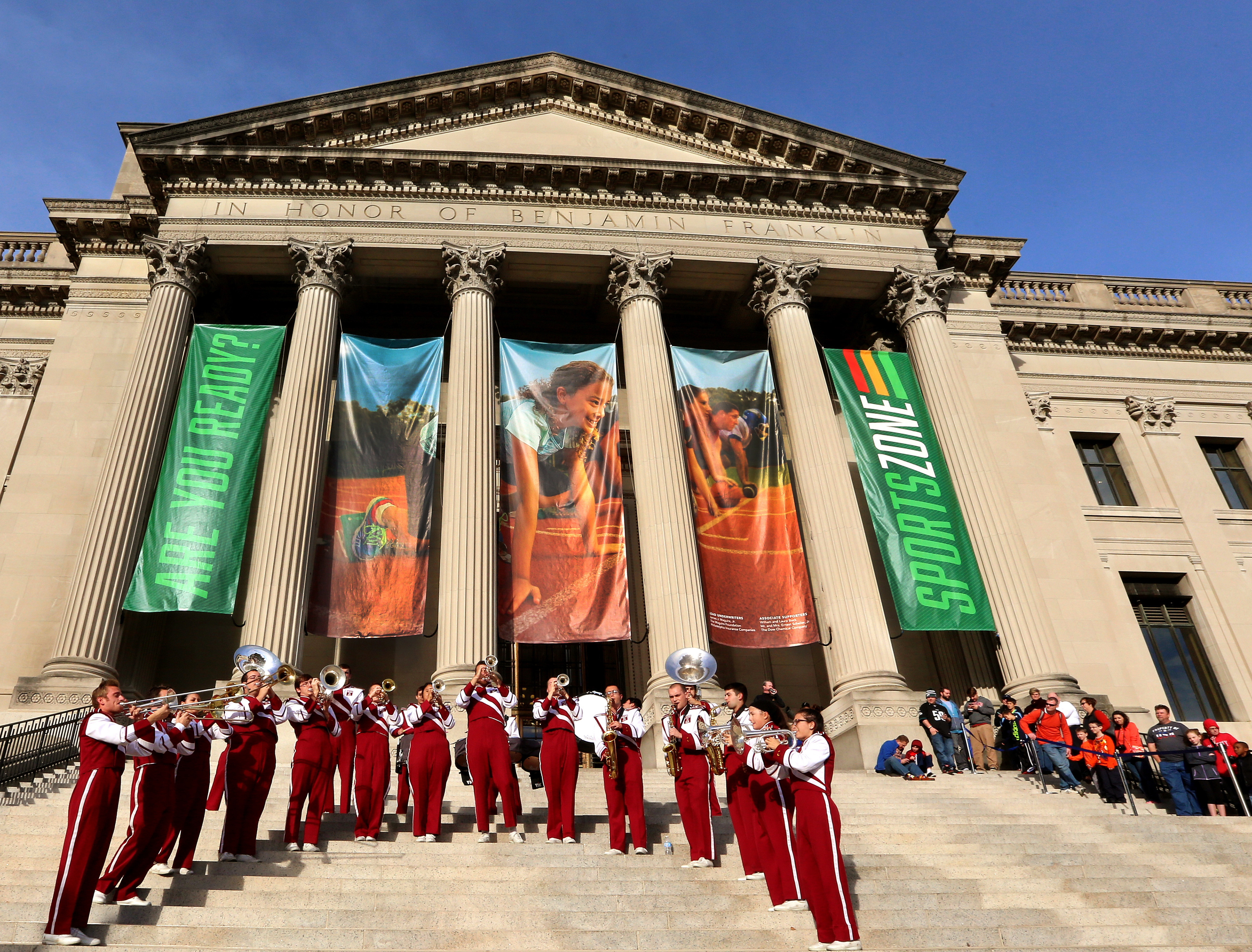 Outside of the Franklin Institute on SportsZone's opening day. There are big banners and a full marching band is playing on the museum steps.