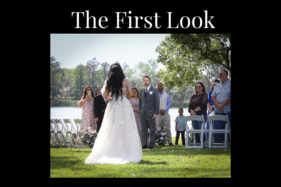 A bride and groom meet eyes at the back of a pew of seats. People stand, clapping and cheering from the pews.