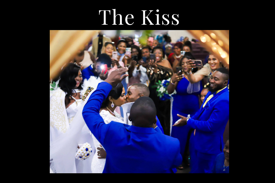 A bride and groom kiss as the wedding party clap and cheer around them.