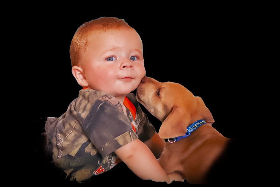 A puppy kisses a smiling infant on the cheek.