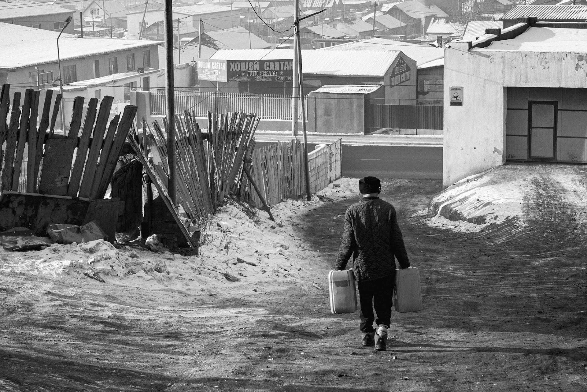 A resident of the Bayanzurkh Ger district carrying containers to a central water kiosk. Ulan Baator, Mongolia, December 2025