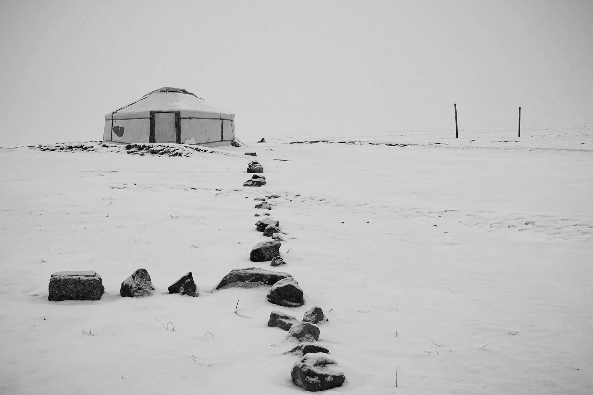 A stone path through the snow leading to the family’s winter camp near the Khongor dunes. Gobi desert, Mongolia, December 2025
