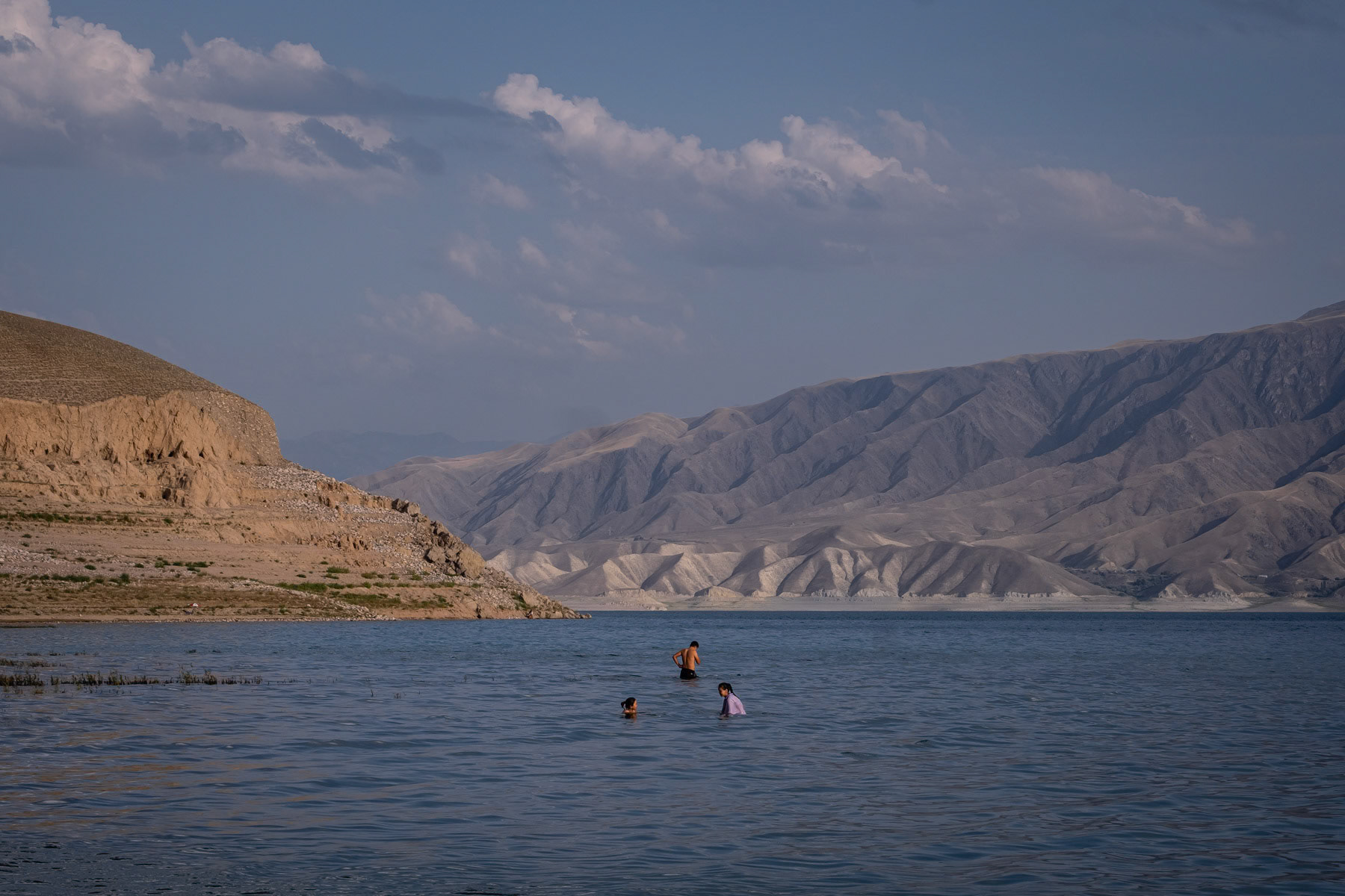 People bathing in the Toktogul Reservoir on the Naryn river on a hot summer day. The reservoir and river are showing alarming low levels following persistent droughts in Central Asia. The hydro electrical power stations on the Naryn river and the Toktogul reservoir are crucial for Kyrgyzstan's energy needs, but with longer and recurring periods of drought it becomes impossible to cater for an ever increasing population. The Naryn river, which in Uzbekistan will become the Syr Daria river and eventually flow into the Aral Sea, has an ever decreasing volume. Further accelerating the complete disappearance of the Aral Sea few thousand km away. Toktogul Reservoir, Kara Kul, Jalalabad region, Kyrgyzstan, August 2021